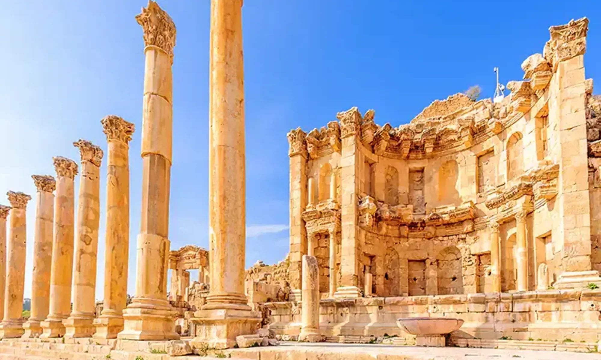 Ancient ruins of a classical building with tall, broken columns and a partially reconstructed wall under a clear blue sky.