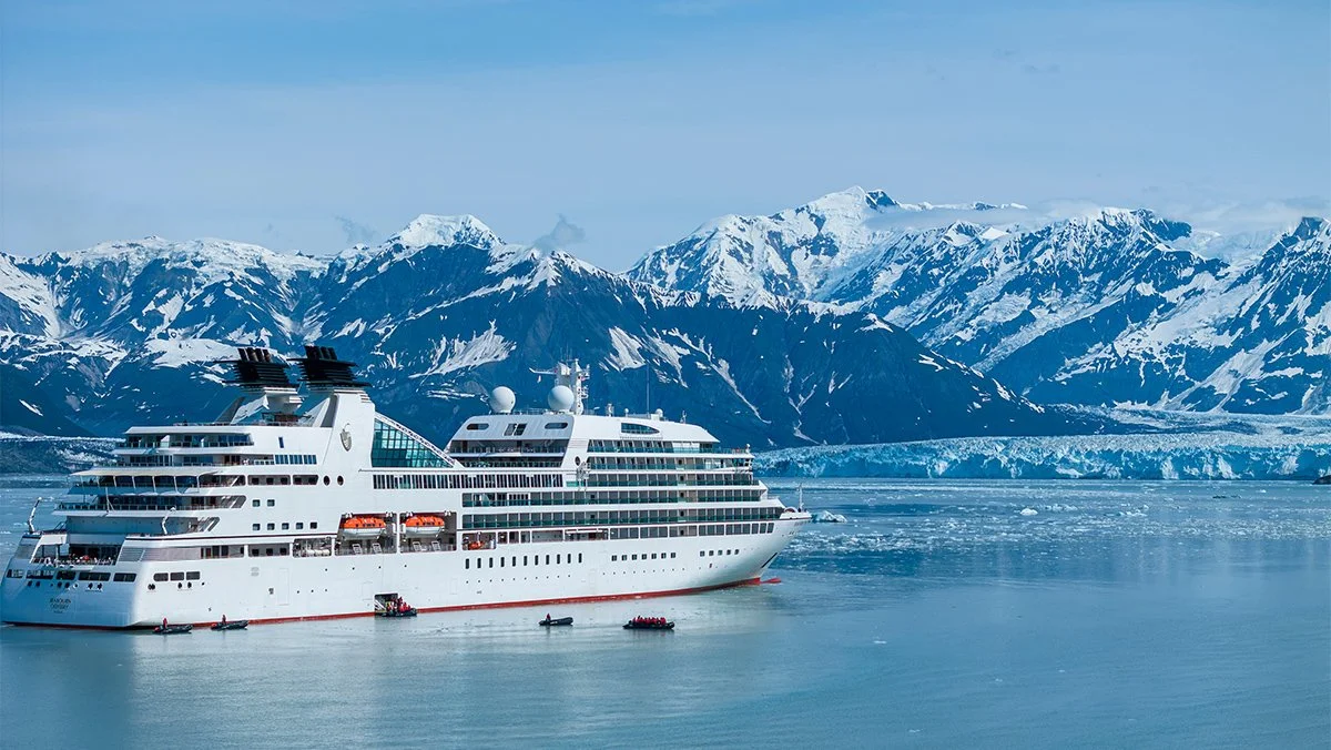 A large white cruise ship sailing in icy waters with snow-covered mountains in the background.
