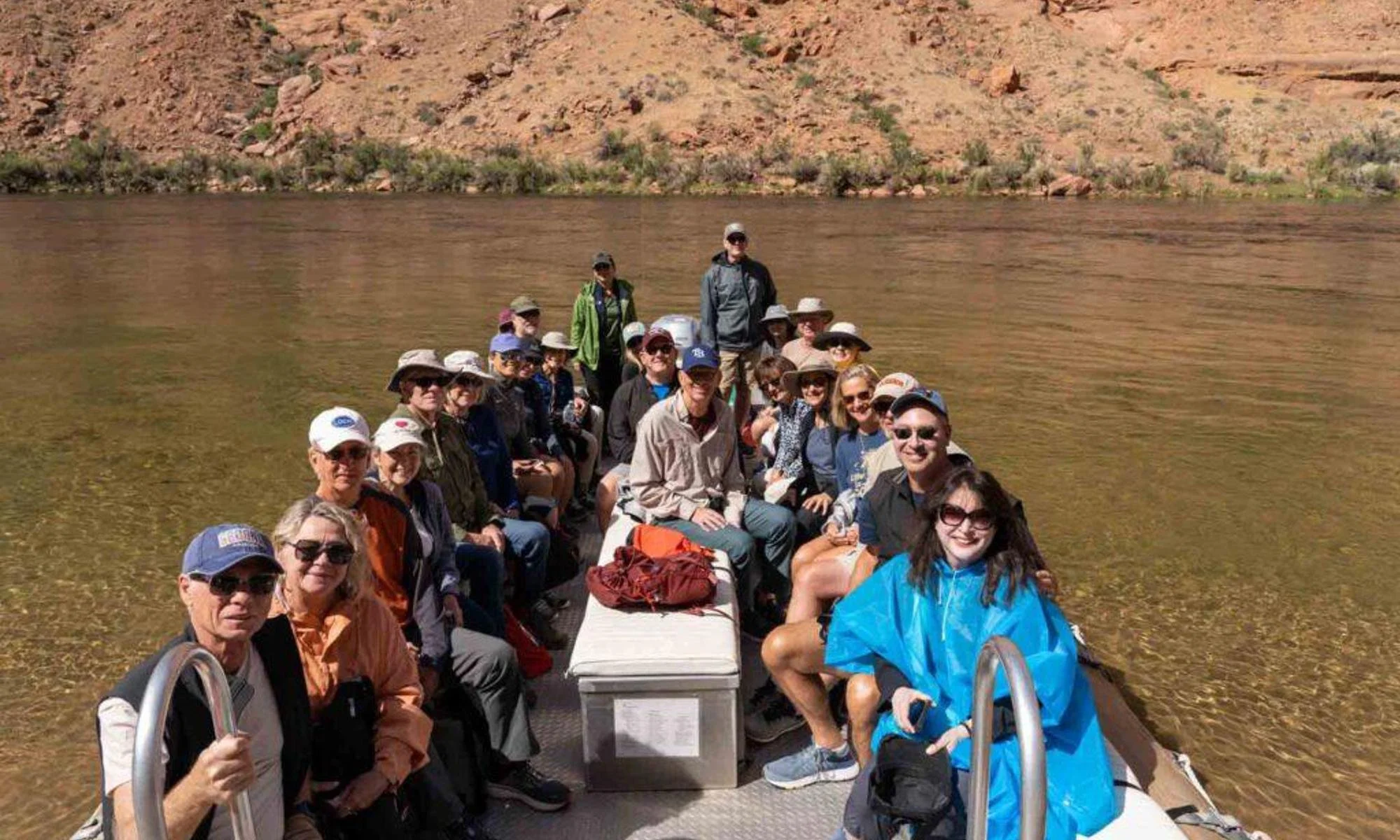 Group of people on a boat in a river, surrounded by rocky, mountainous terrain with sparse vegetation.