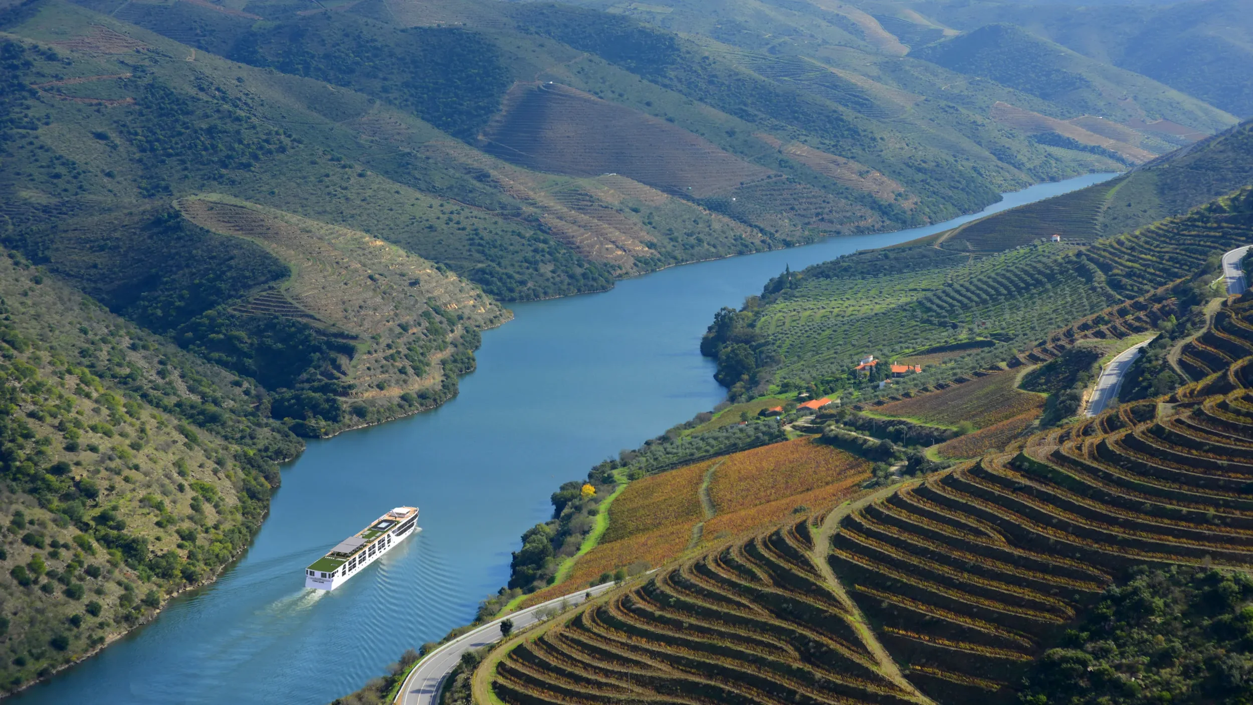 A river winding through a lush green valley with terraced vineyards on the hillside, and a large white boat sailing on the water.