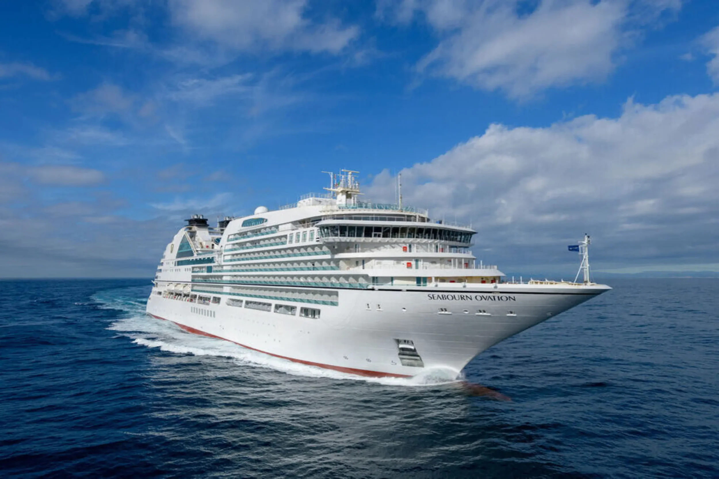 Large white cruise ship named Seabourn Ovation sailing in the ocean under a partly cloudy sky.