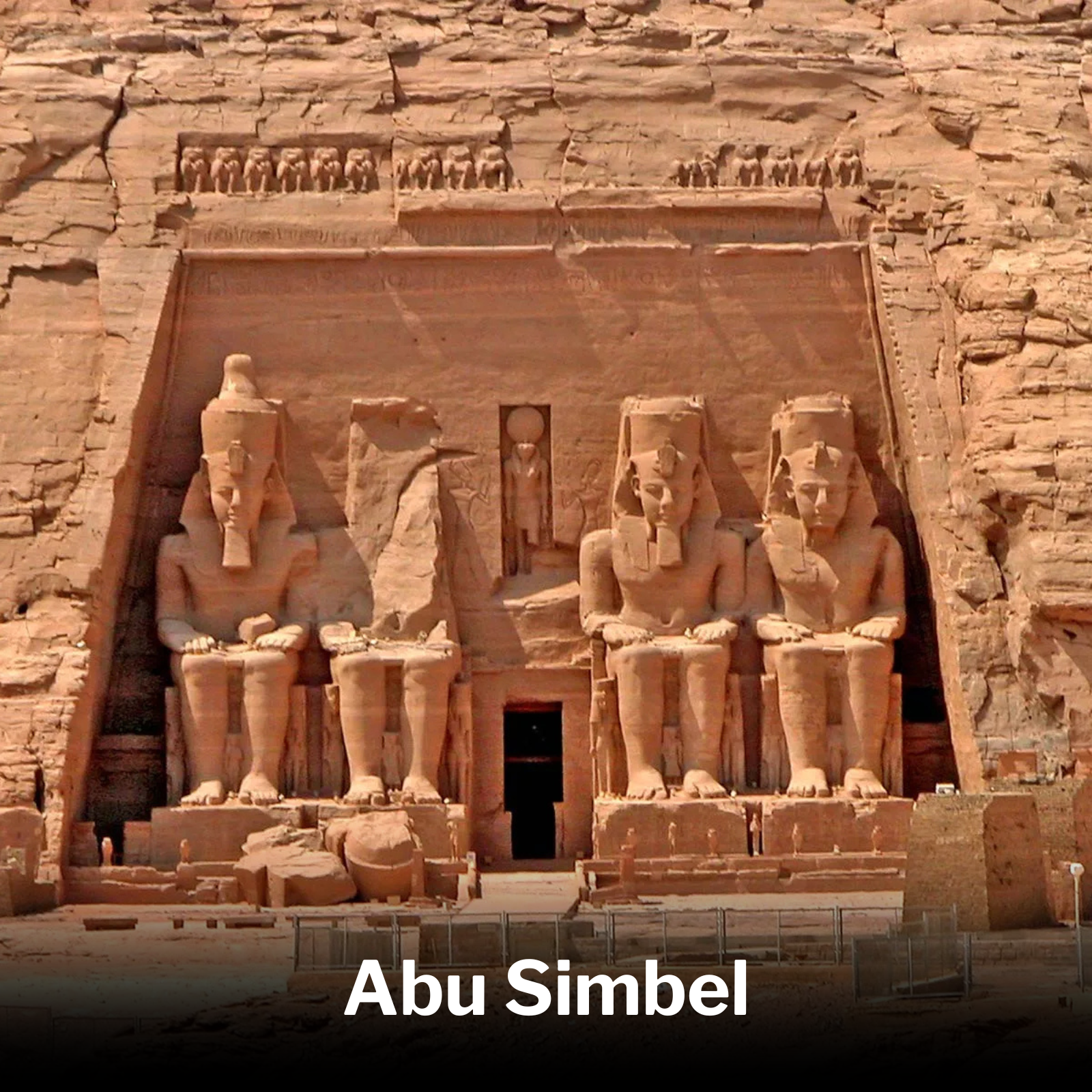 Ancient Egyptian temple entrance with four large seated statues of Abu Simbel, carved from stone, with hieroglyphic carvings and smaller statues in the background.
