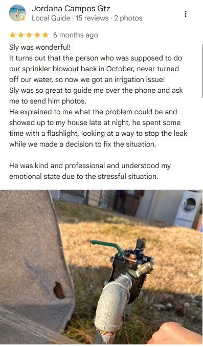 A yard with grass and an outdoor utility box, and part of a person’s hand and sprinkler pipe in the foreground.