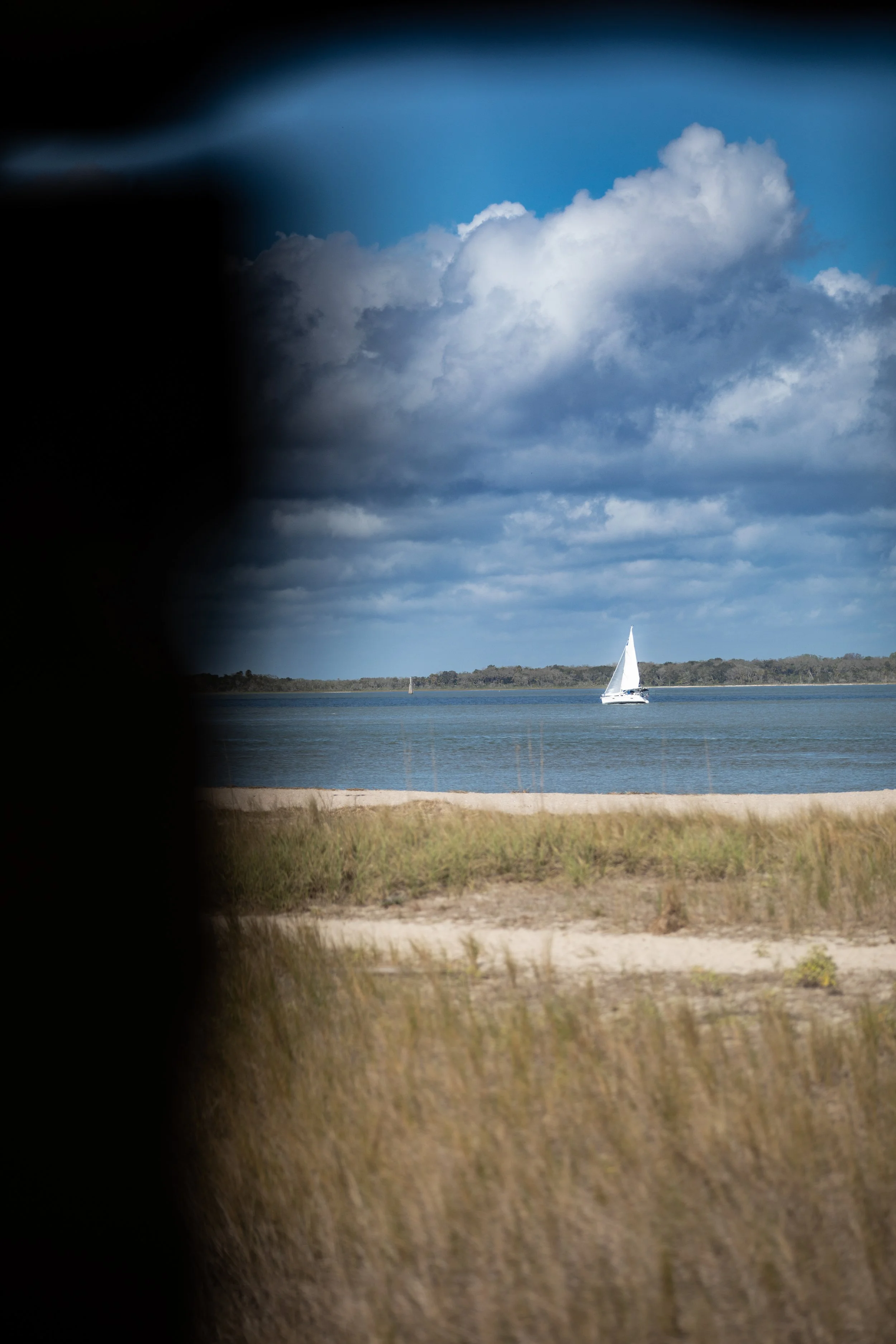 A sailboat on calm water with a cloudy sky above and distant shoreline.