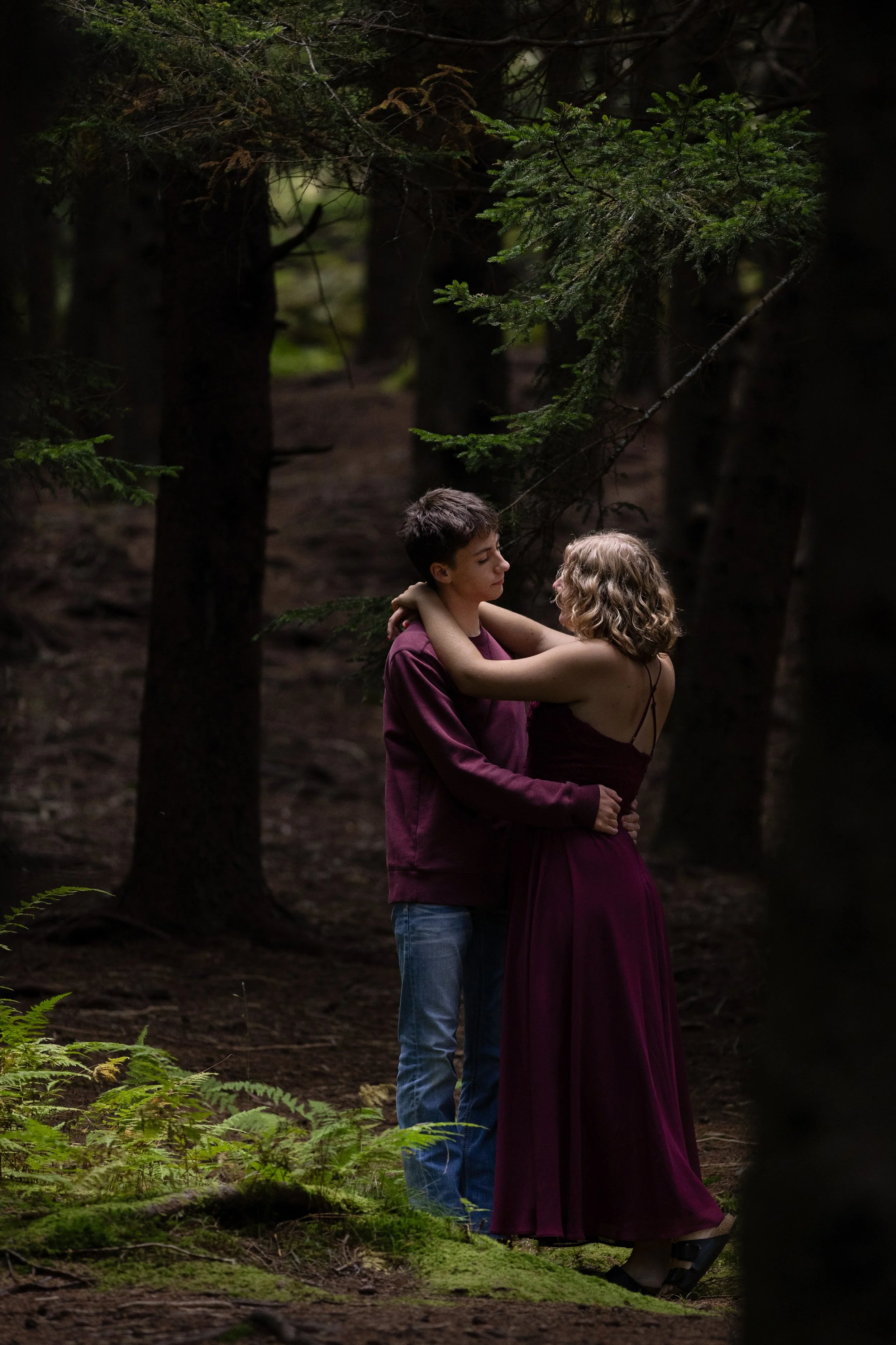 A young man and woman embracing and looking into each other's eyes in a forest.
