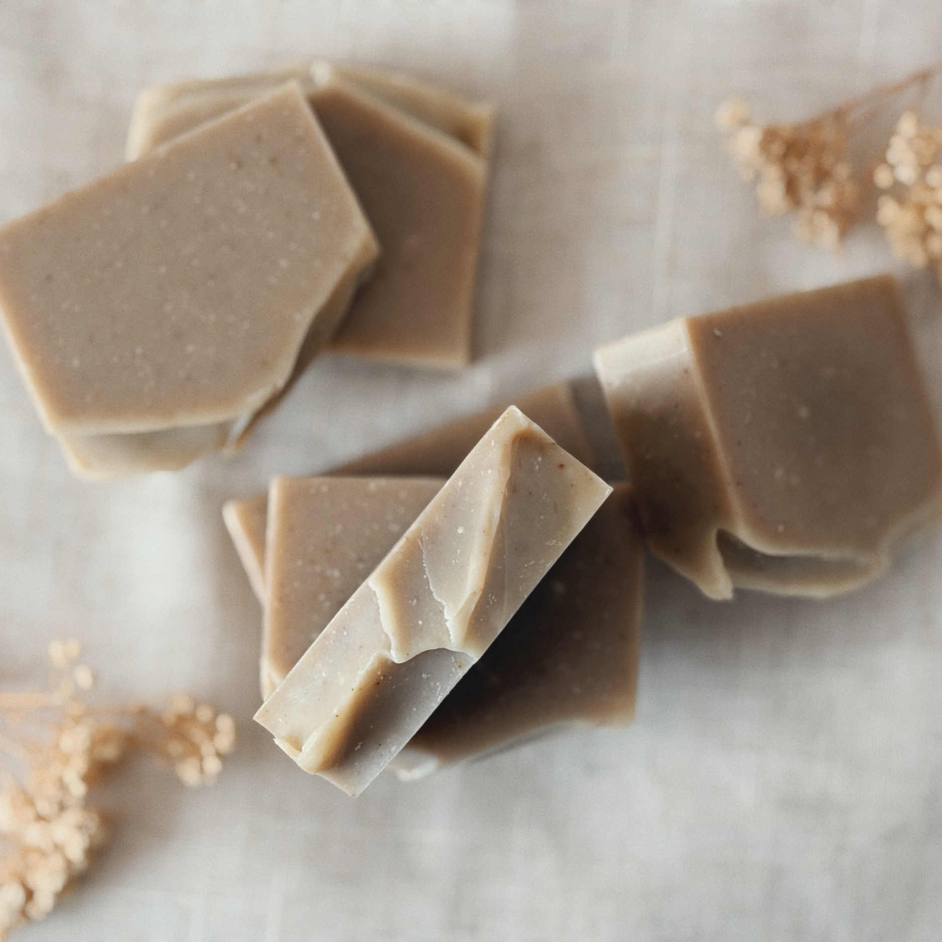 Close-up of beige soap bars with a smooth surface, arranged on a light-colored surface with some crumbs around.