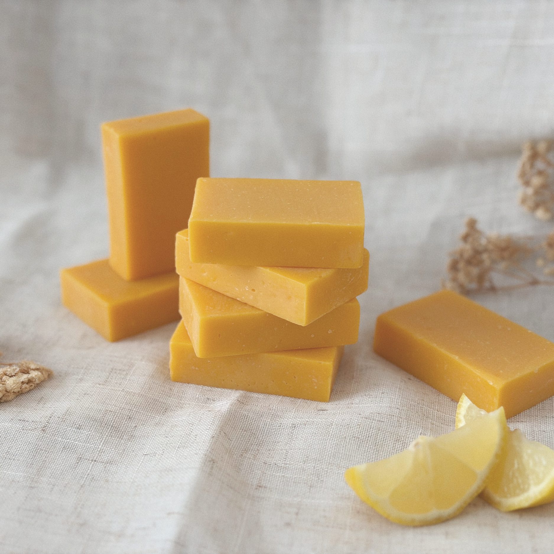 Slices of yellow cheese stacked on a white cloth with lemon and grain on the side.