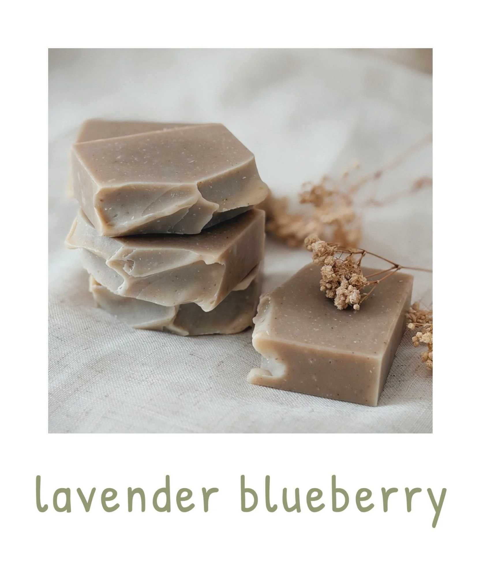 Close-up of stacked lavender blueberry soap bars with dried lavender and blueberries on white cloth background.