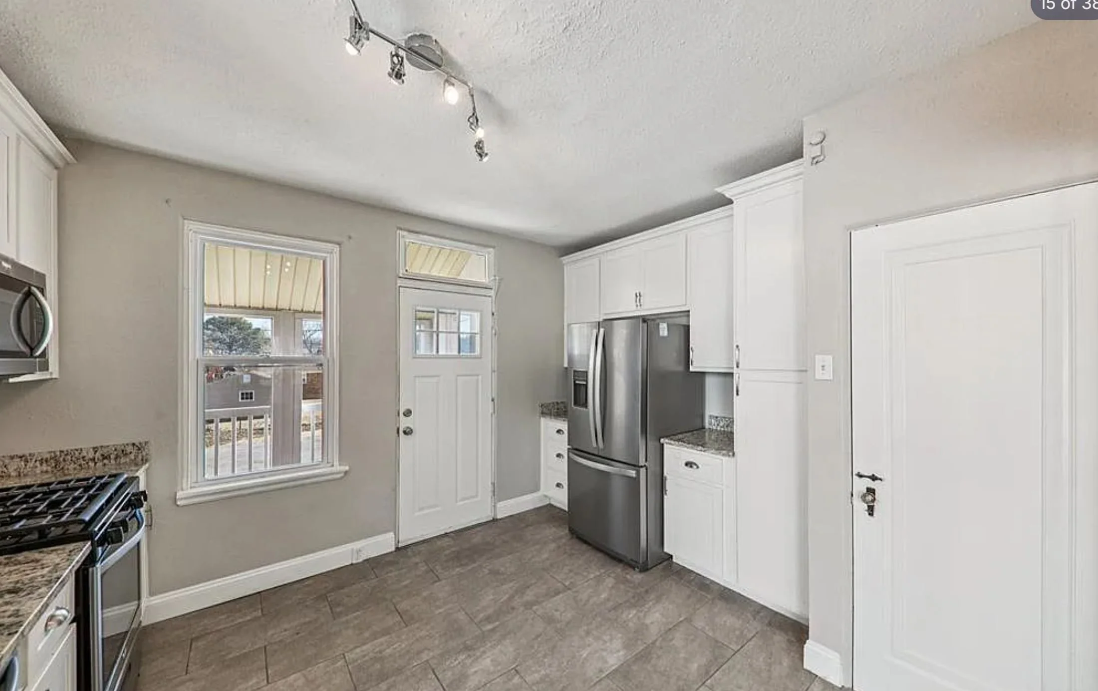 Kitchen featuring white cabinets, stainless steel refrigerator, granite countertops, and a window overlooking a porch area.