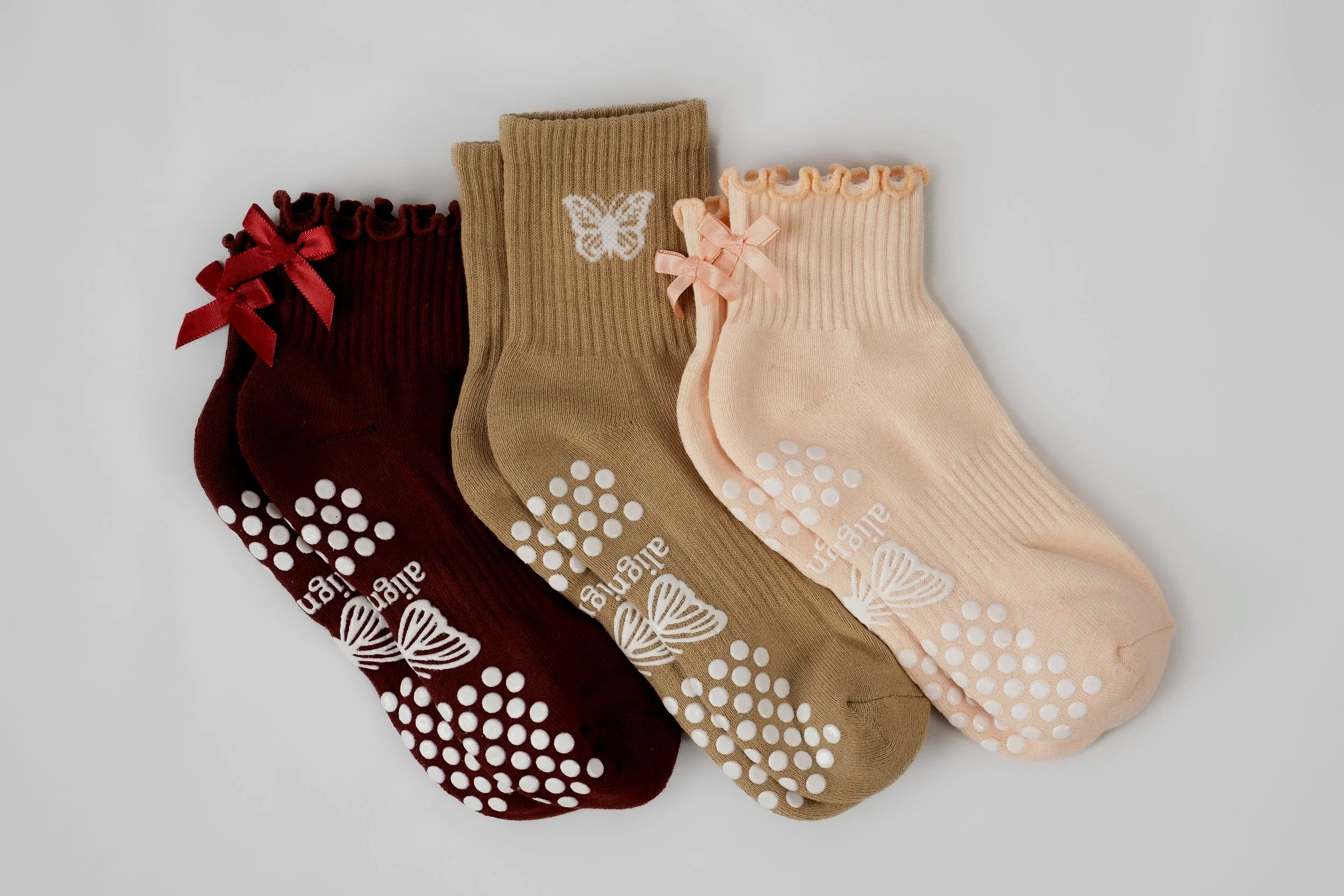 Three pairs of align&co. organic cotton Pilates grip socks in burgundy, tan, and light pink with feminine bow and butterfly details.
