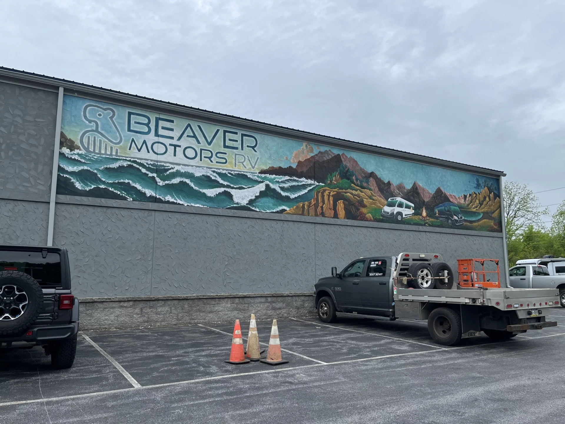 Large mural on a building wall showing a landscape with mountains, ocean waves, and a camper with mountains, trees, and a campsite in the background. The mural includes the text 'Beaver Motors RV' and a beaver logo.