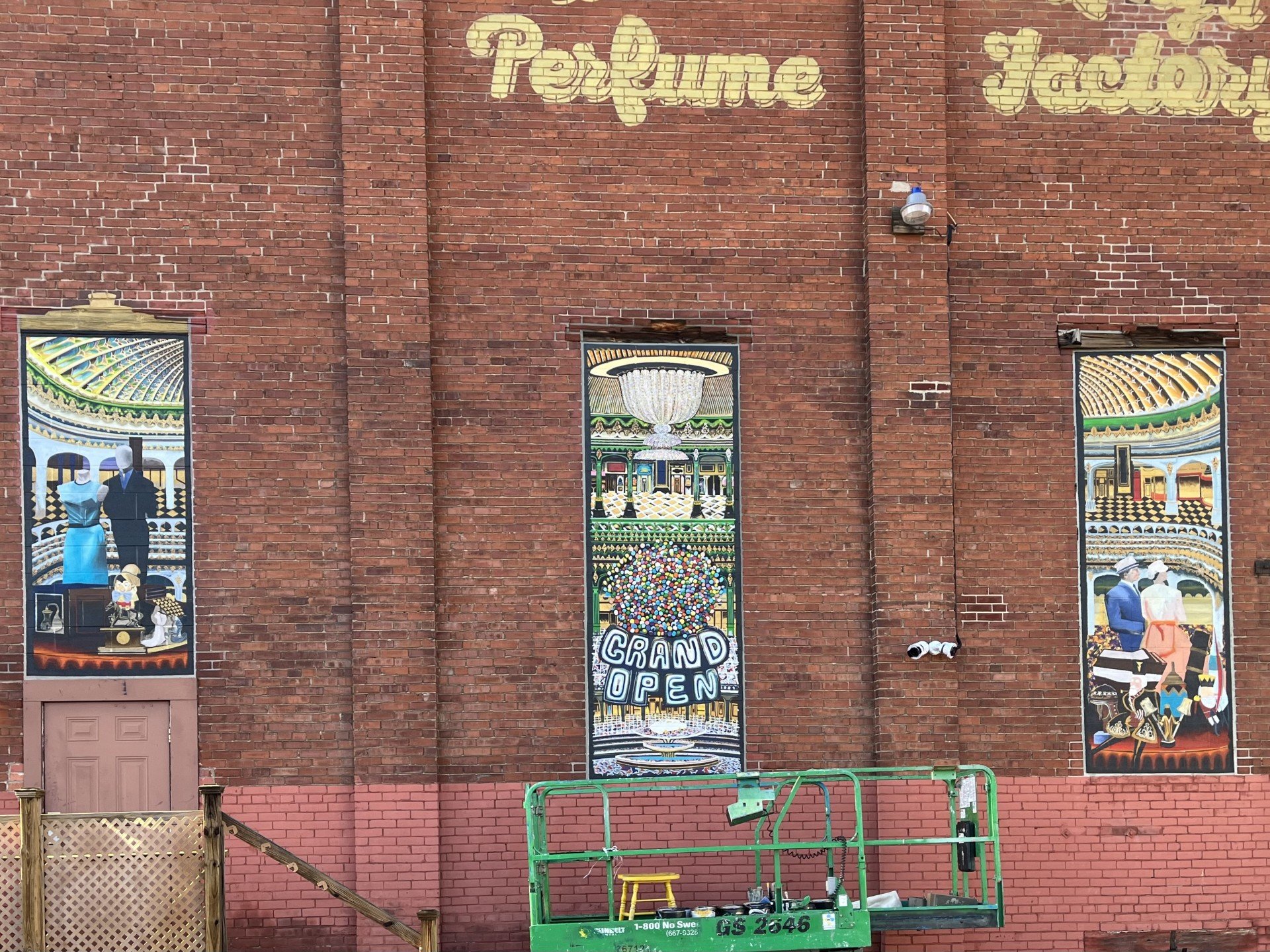 Three brightly colored stained-glass panels depicting vintage scenes on a brick building with painted words 'Treasure' and 'Grand Open'.