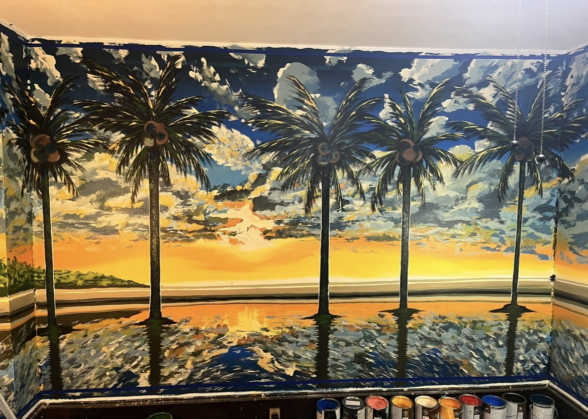 Wall painting of a sunset over a tropical beach with palm trees reflected in the water.
