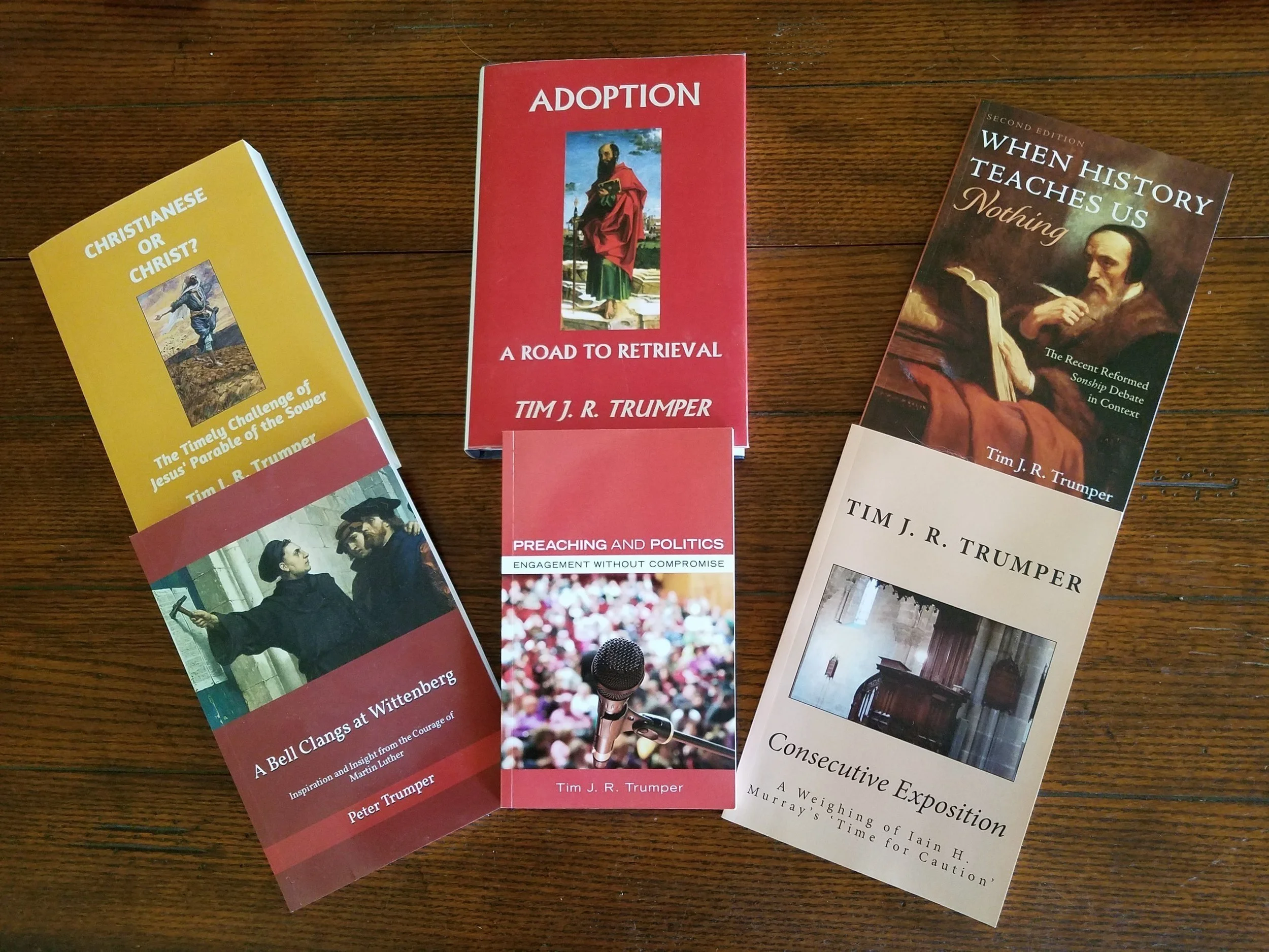 Three books on a wooden surface, with titles about religion, politics, history, and preaching, each featuring different covers and colors.