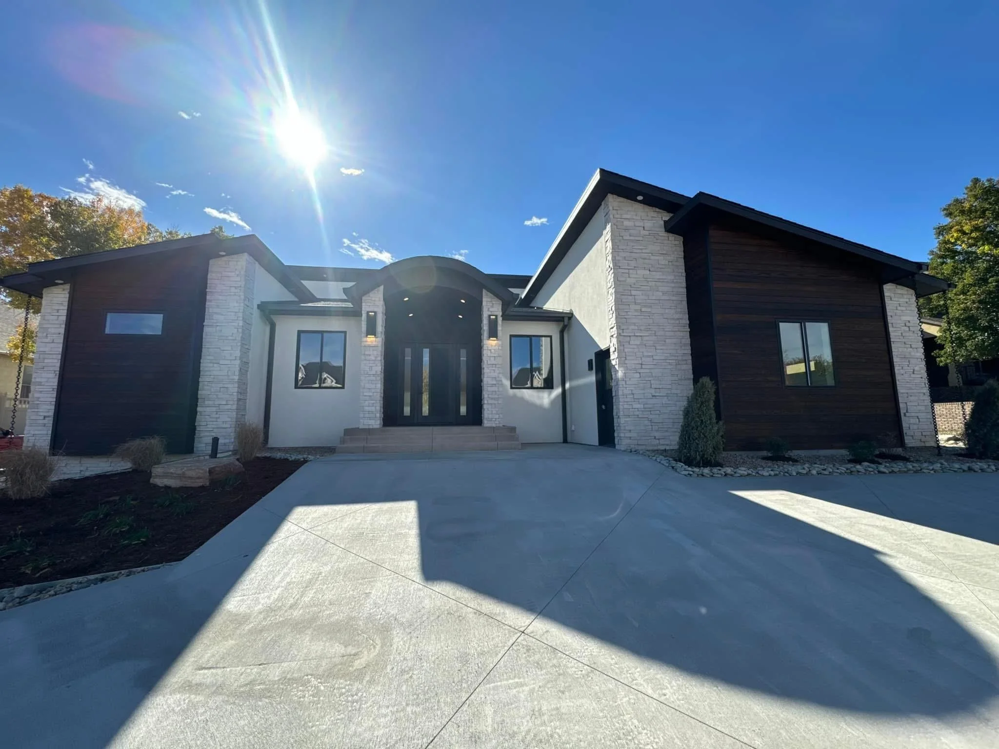 A modern house with black and white exterior, large windows, and a concrete driveway under a sunny blue sky.