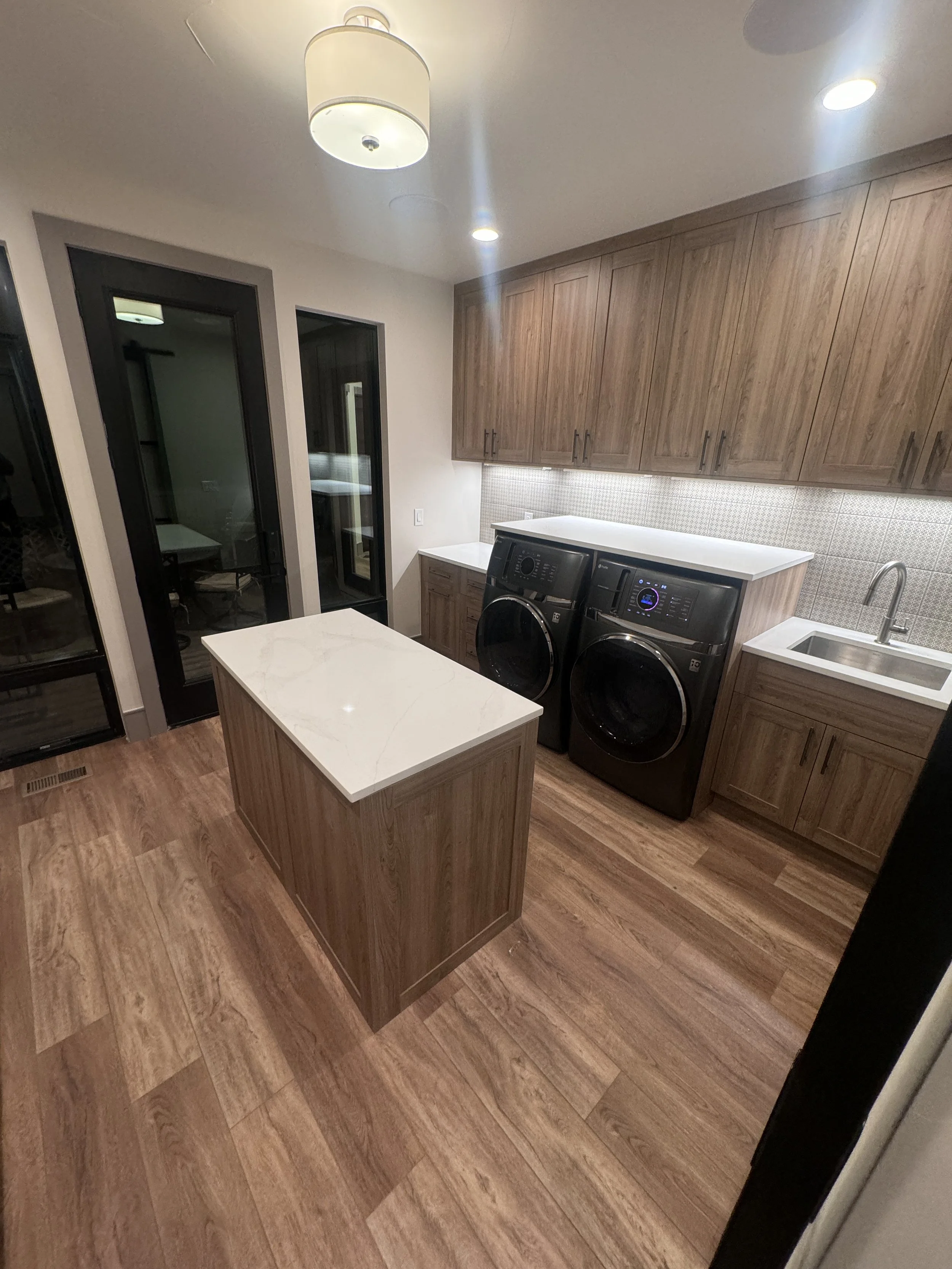 A laundry room with wooden cabinets, a white countertop, a wash machine and dryer, a small sink, and sliding glass doors.