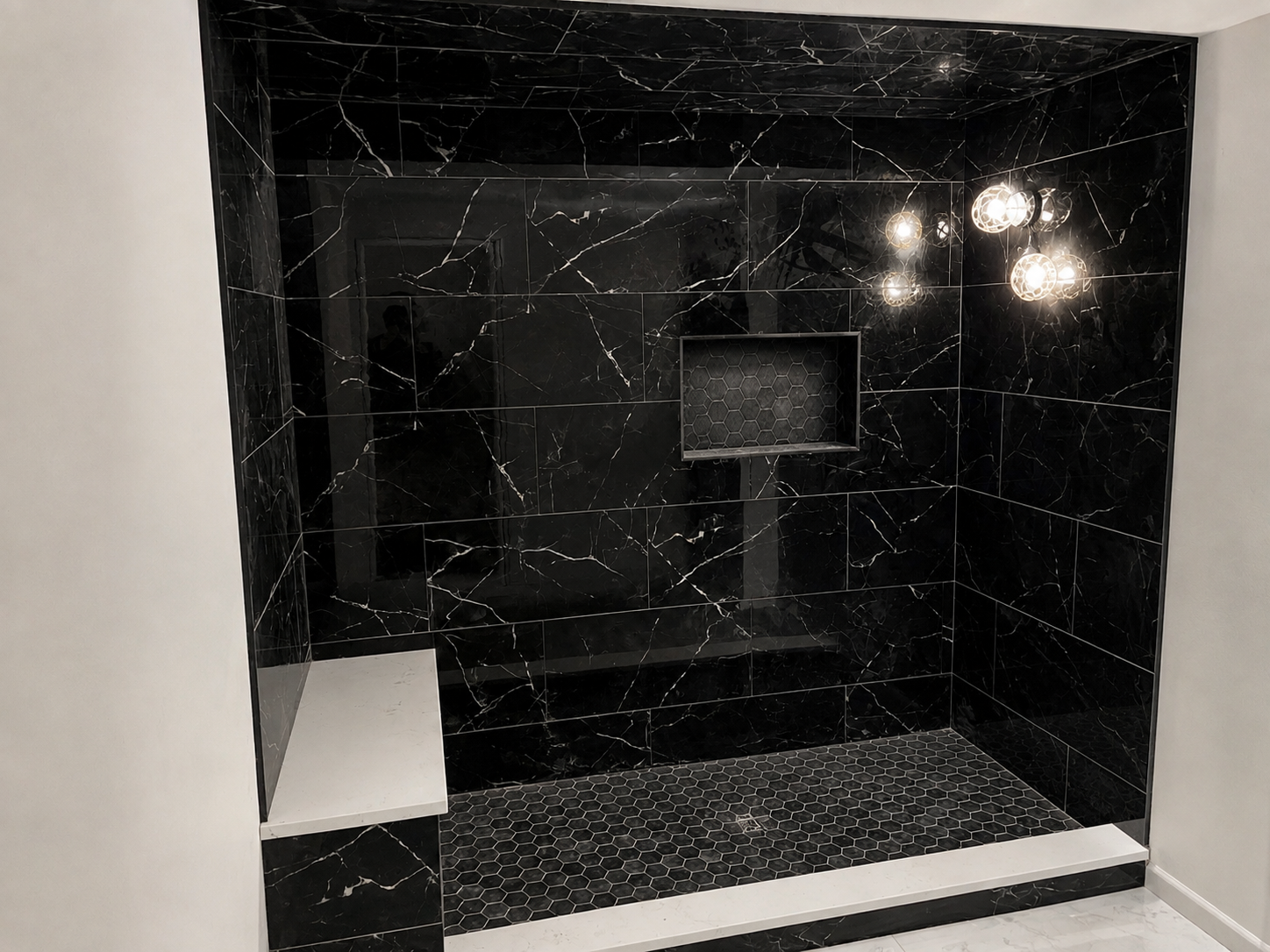 Shower with black marble tiles, hexagonal black tile flooring, and modern light fixture with multiple exposed bulbs.