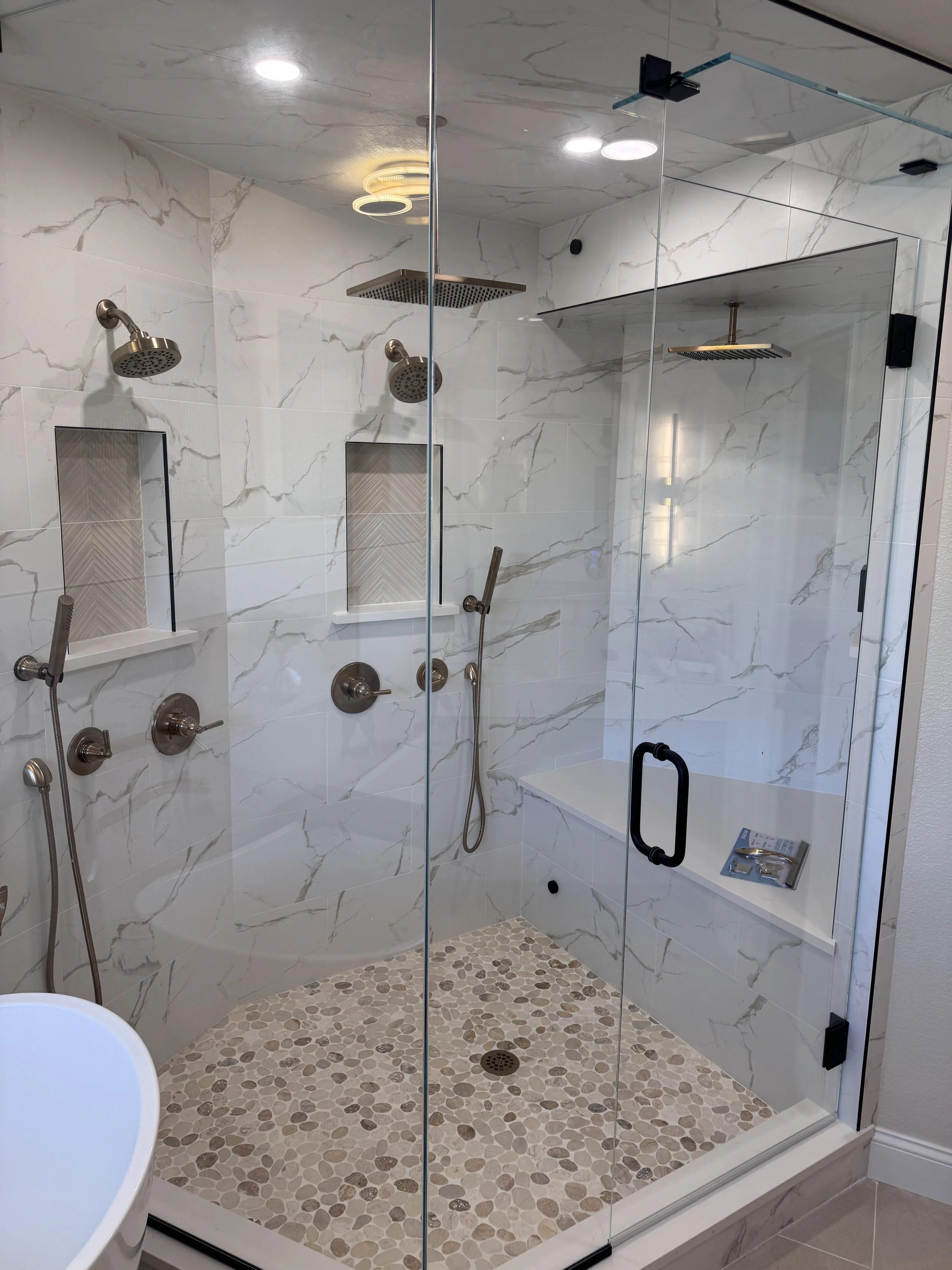 Modern walk-in shower with marble tile walls and pebble stone shower floor, featuring multiple shower heads and a glass partition.