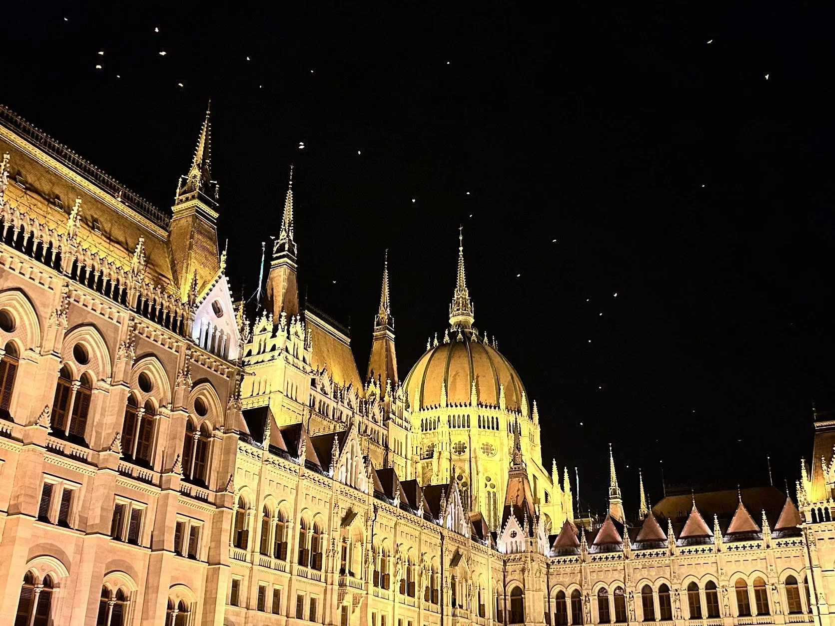 Night view of the illuminated Parliament building with tall spires and a large domed roof, set against a dark night sky with visible stars.