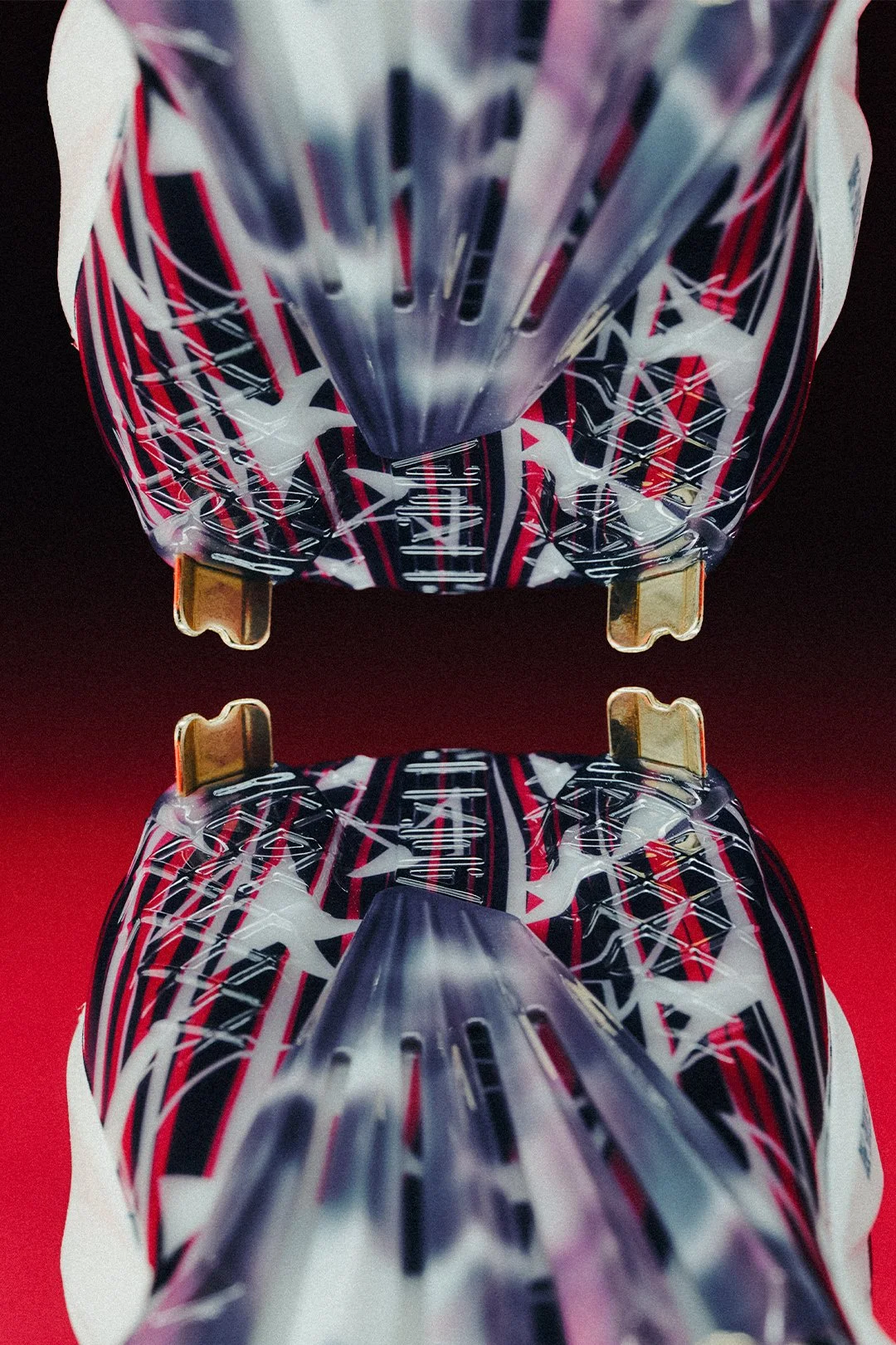 A close-up photograph of two chocolate bars, stacked vertically, with the camera focusing on the middle section where the bars meet. The wrapper has a geometric pattern with black, red, white, and gray colors, and the bars are partially unwrapped, re