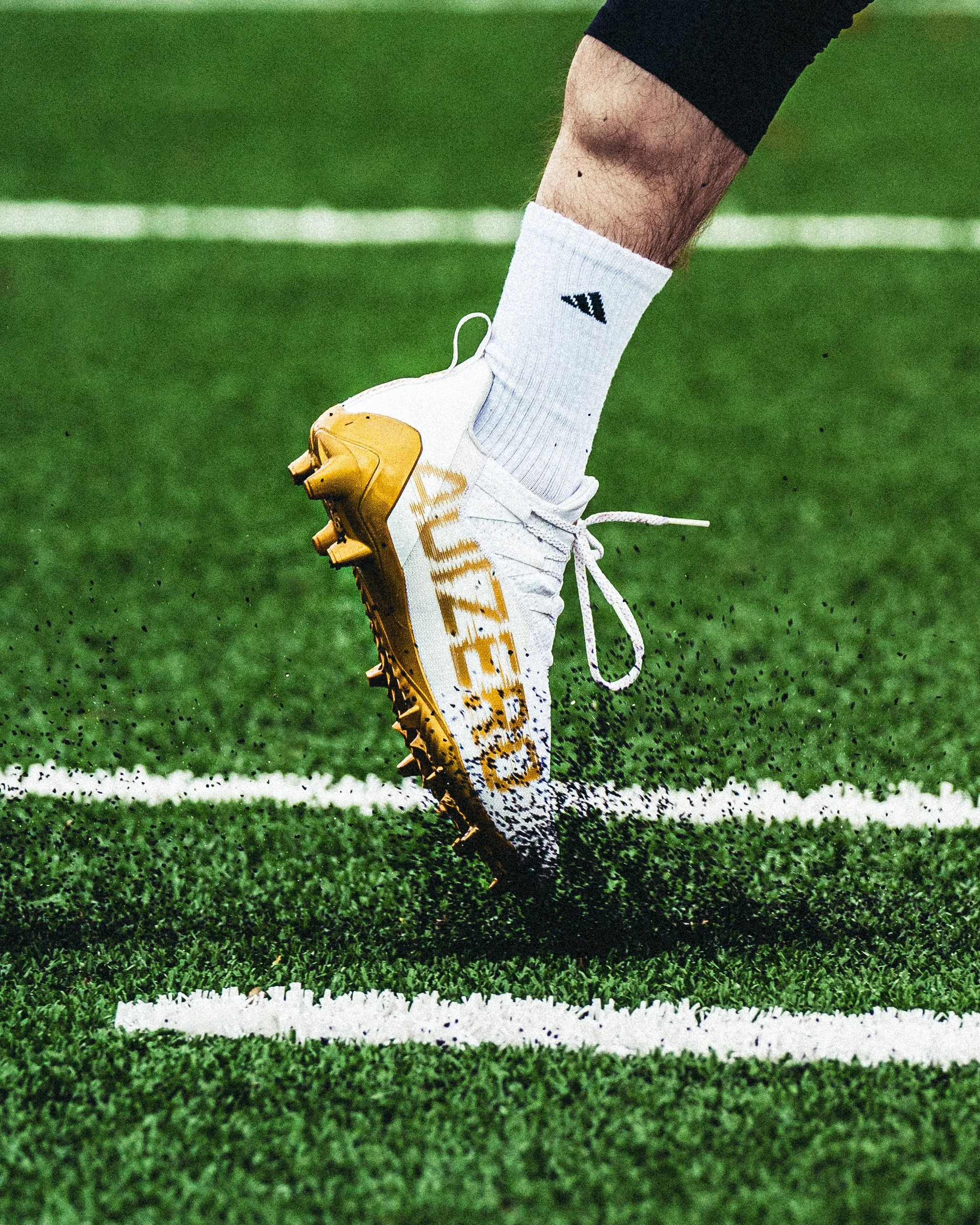 Close-up of a sports shoe on a grass field with white boundary line, as a person appears to be kicking or running.