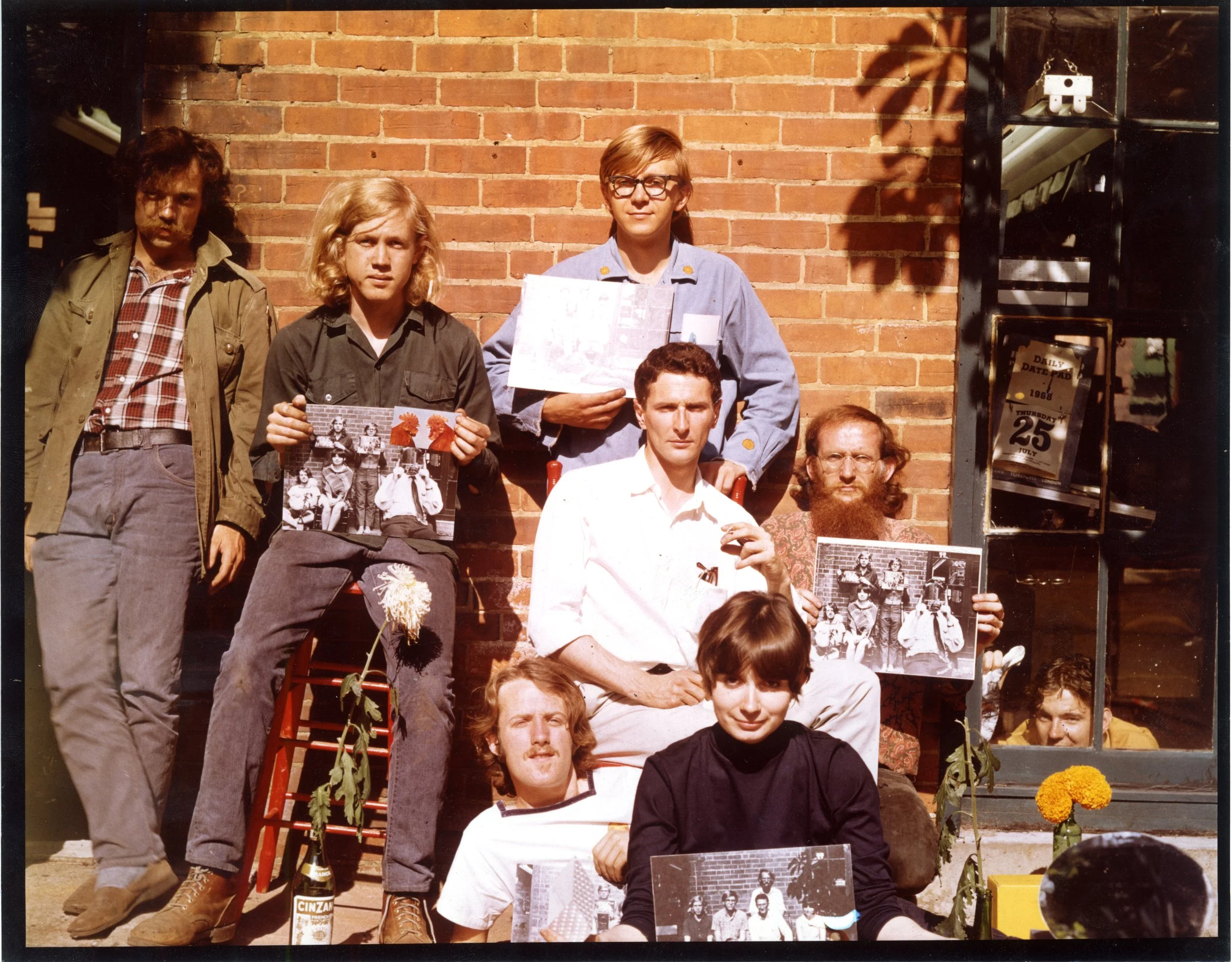 photo of Coach House crew in 1968 outside against a brick wall holding photos of staff shoots in same location