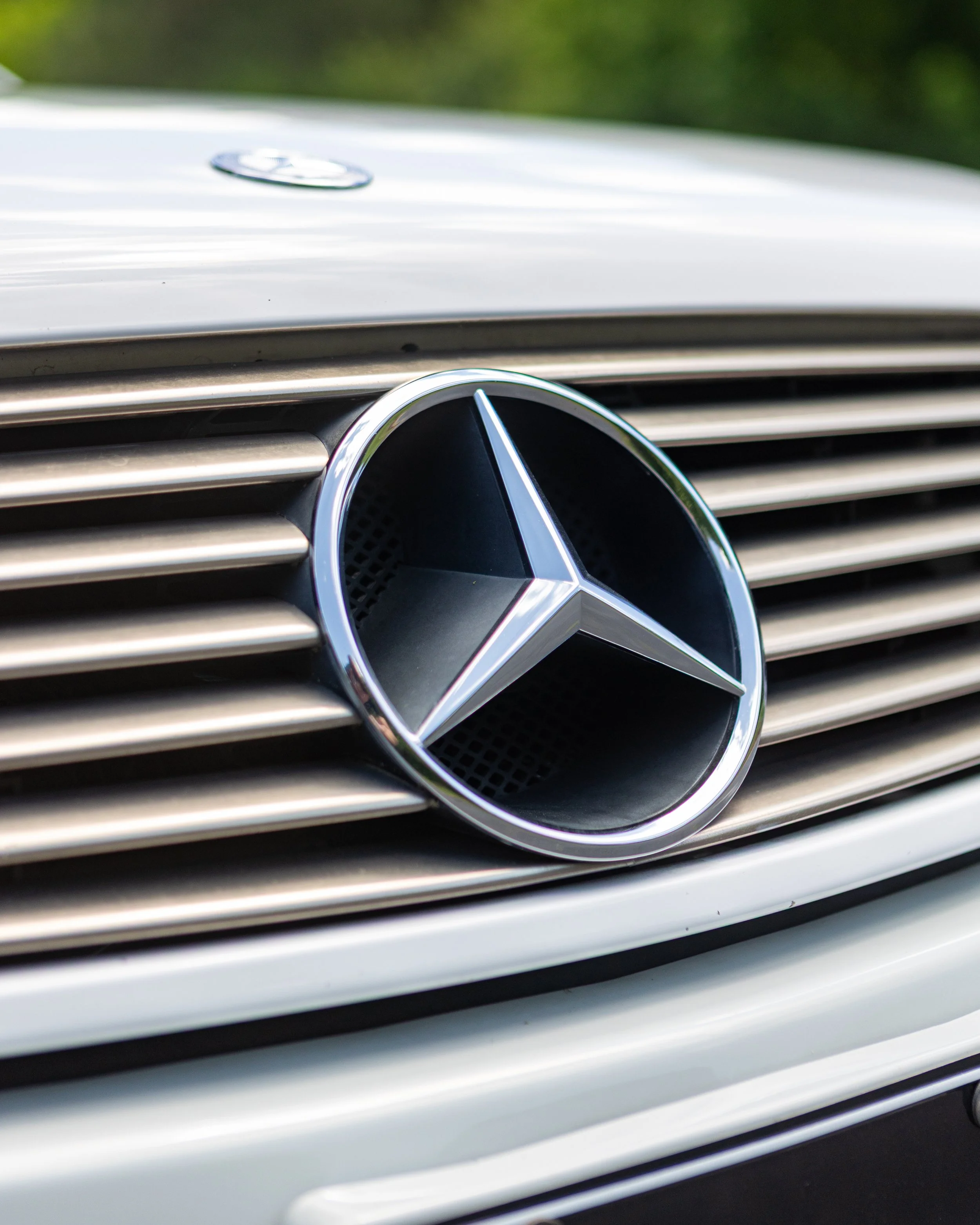 Close-up of a silver Mercedes-Benz logo on the front grille of a car.