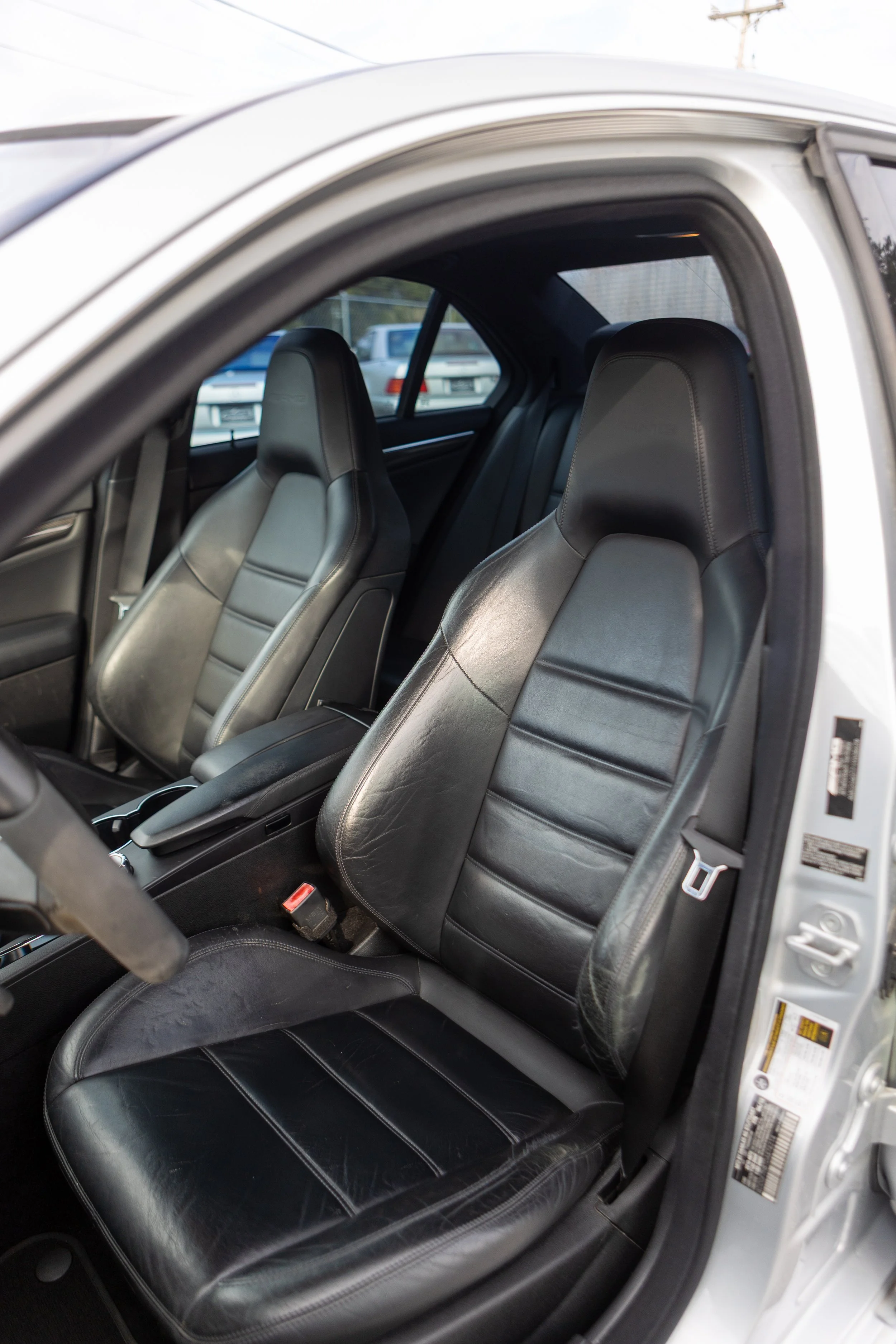 Interior of a luxury Mercedes-Benz vehicle showcasing the dashboard, steering wheel, and front seat, with a modern building visible through the windshield.