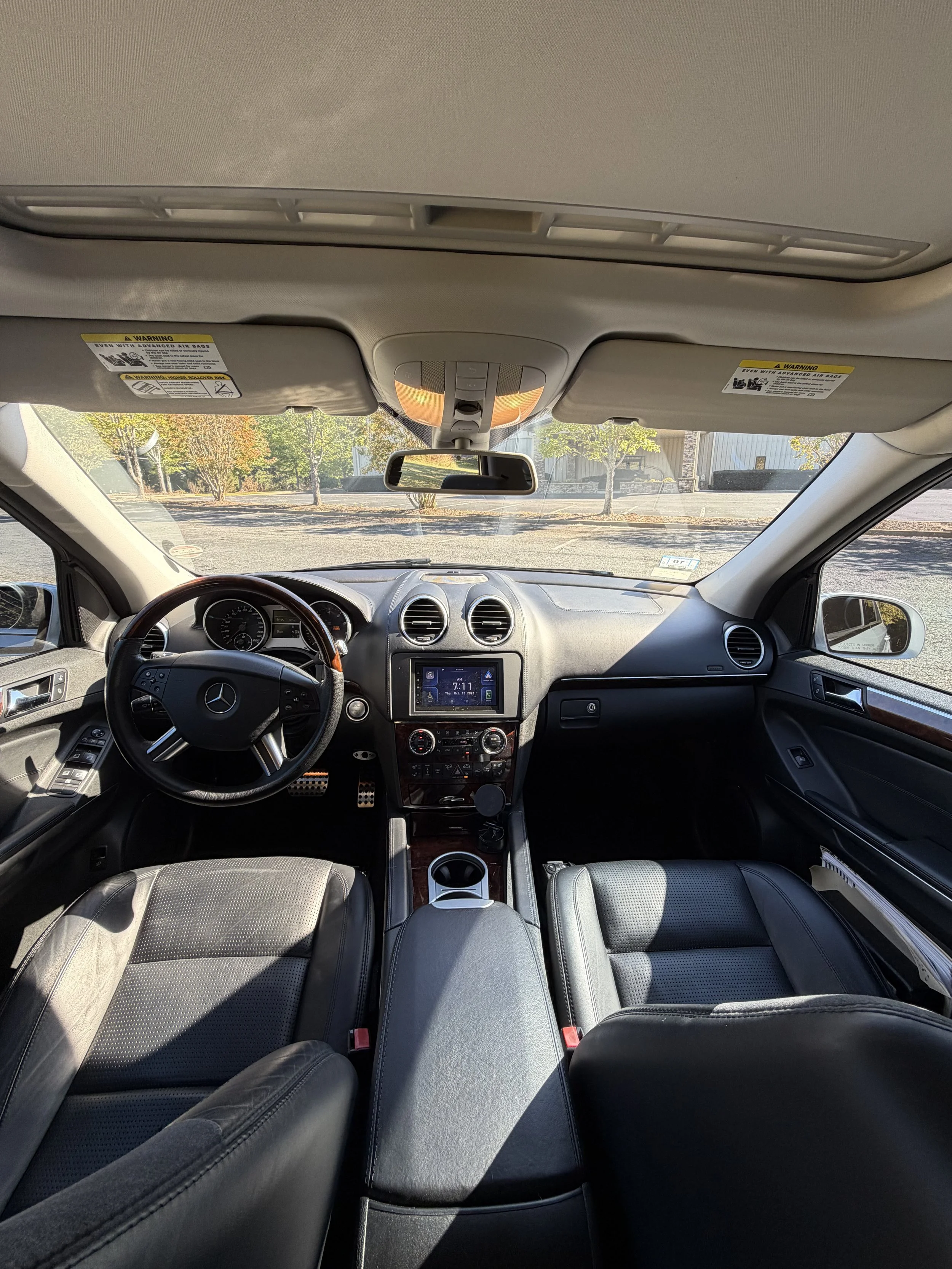 Interior of a luxury Mercedes-Benz vehicle showcasing the dashboard, steering wheel, and front seat, with a modern building visible through the windshield.
