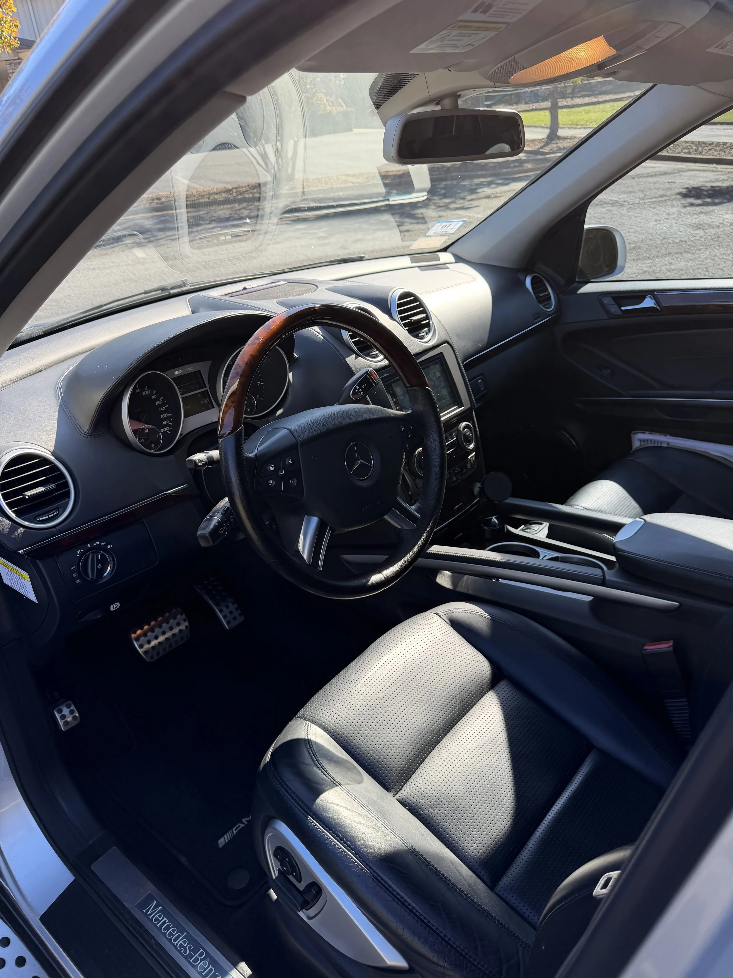 The interior of a vehicle showing black leather seats with perforated patterns and headrests, and a rear window with a view of a concrete wall and cloudy sky.