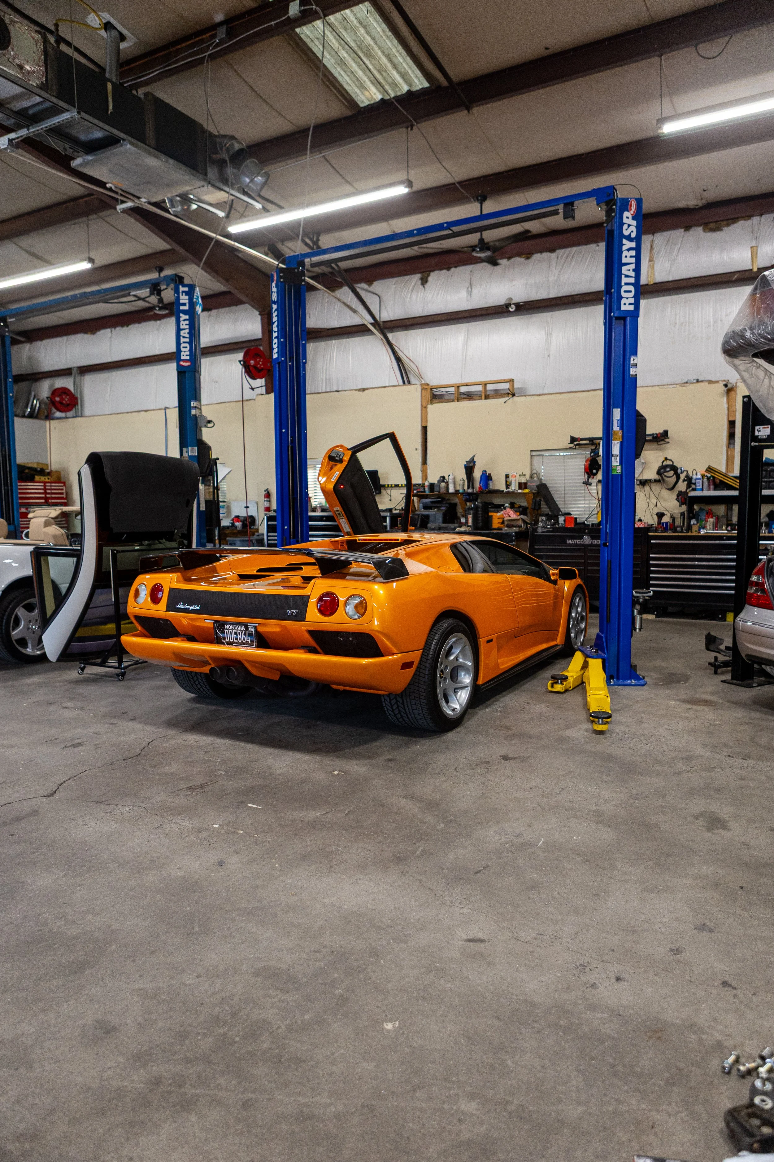 Orange Lamborghini sports car in a garage dedicated to car maintenance and repair, with workshop tools and equipment visible.