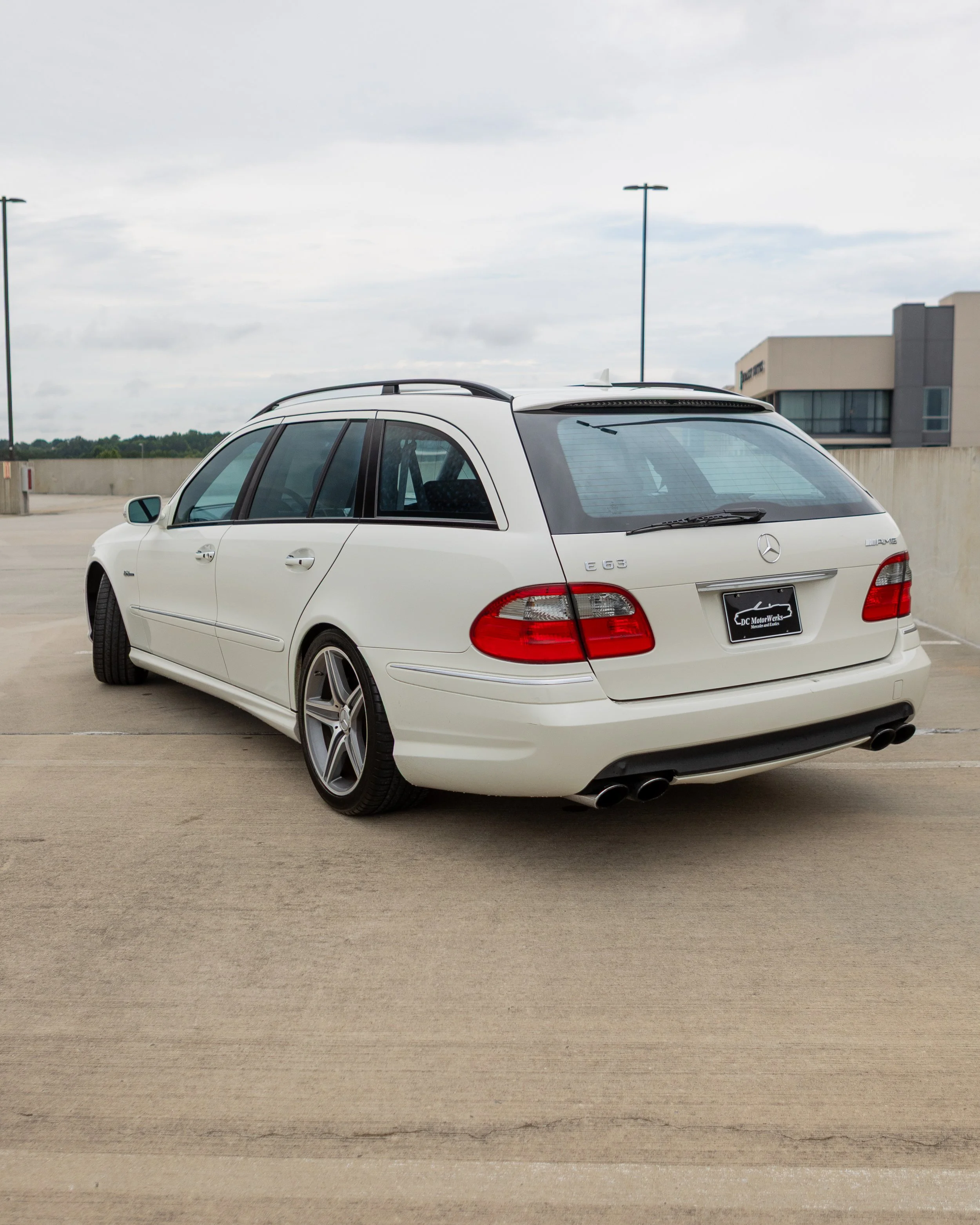 White Mercedes-Benz E 63 AMG station wagon parked on a rooftop parking lot, with a gray building and overcast sky in the background.