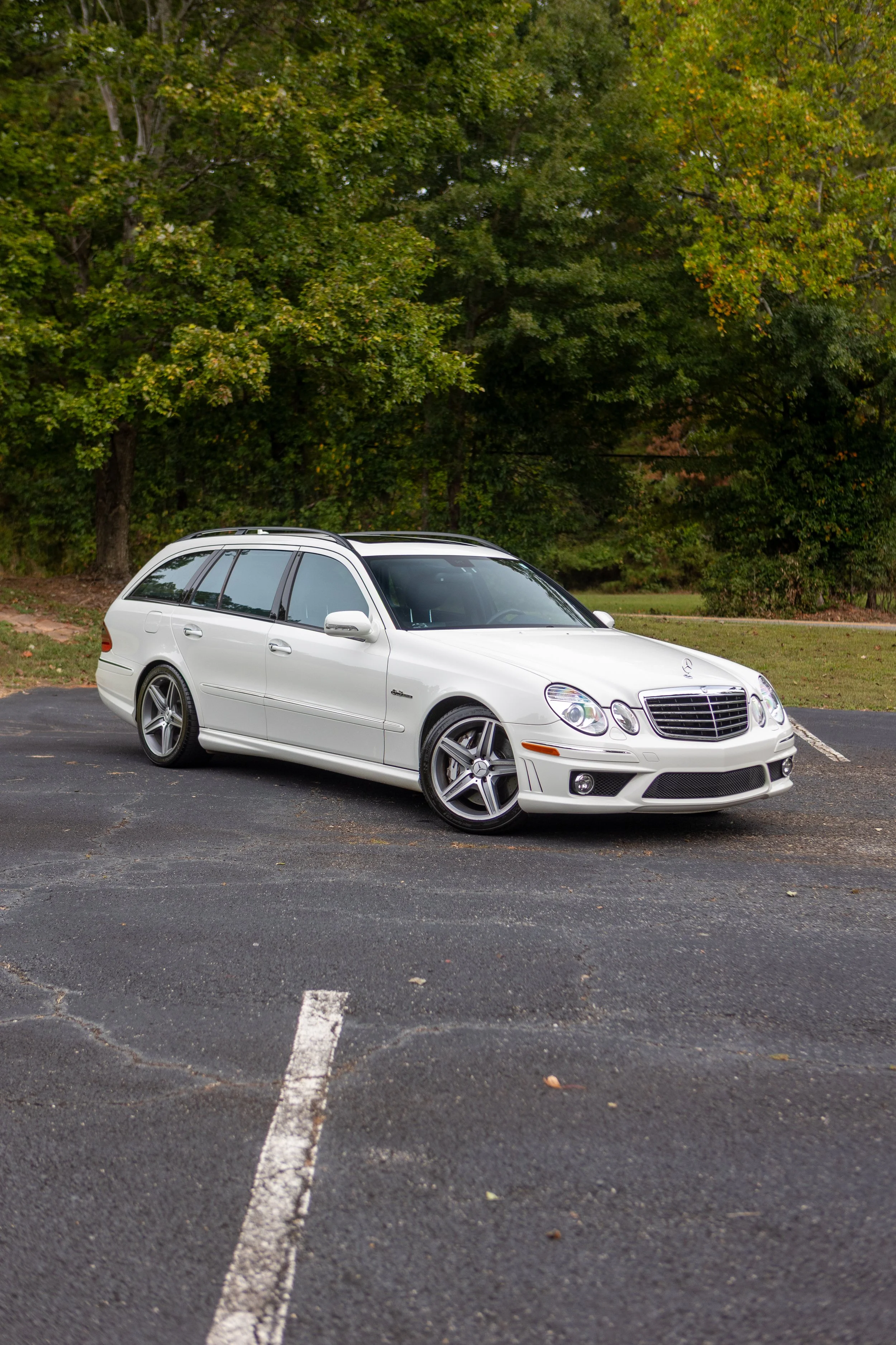 A white luxury sedan car parked on the top level of a parking garage, under a cloudy sky, with some trees visible in the background.