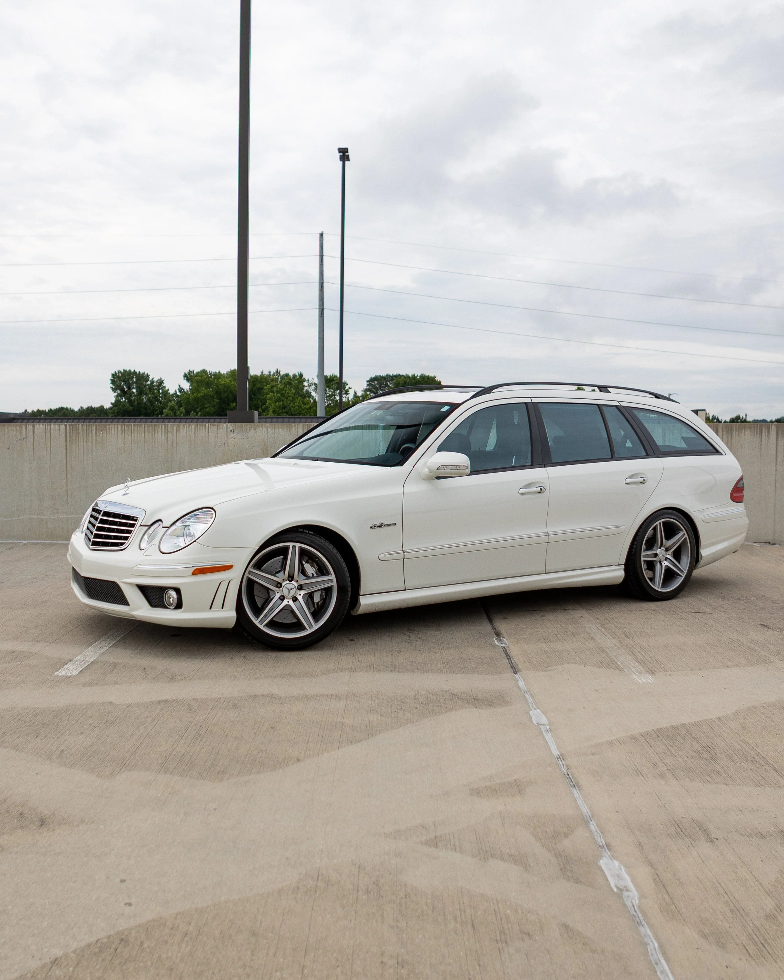 A white luxury sedan car parked on the top level of a parking garage, under a cloudy sky, with some trees visible in the background.
