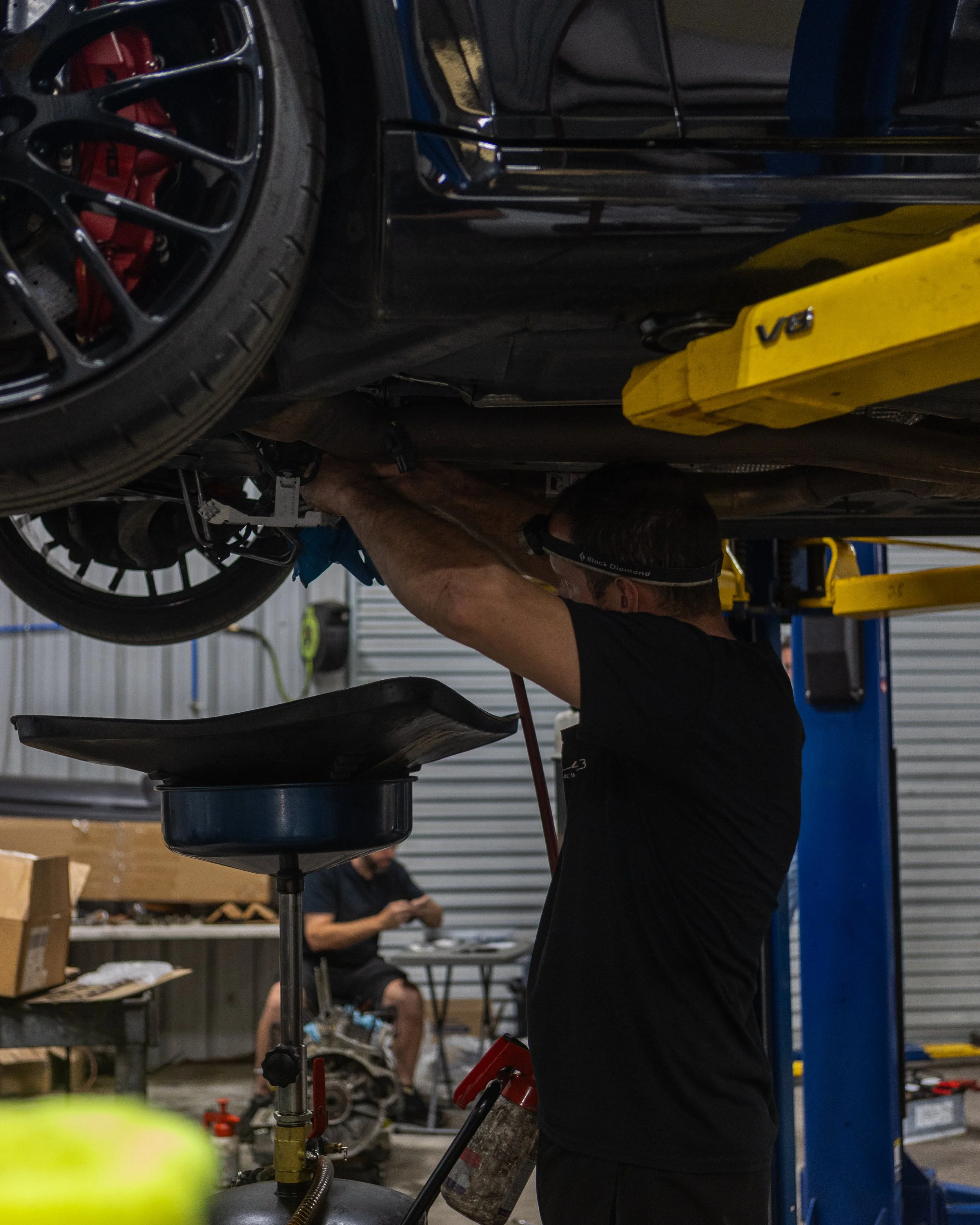 An auto mechanic working under a vehicle on a lift in a garage, with tools and equipment around.