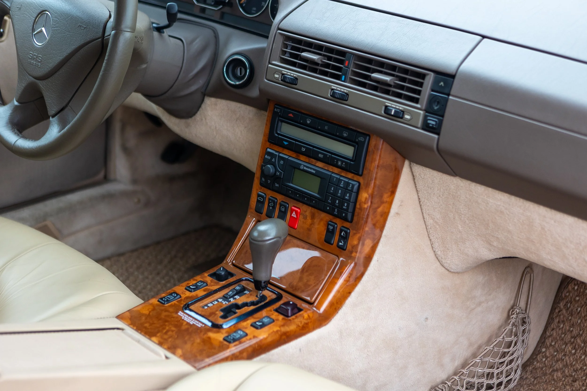 The interior of a vehicle showing black leather seats with perforated patterns and headrests, and a rear window with a view of a concrete wall and cloudy sky.