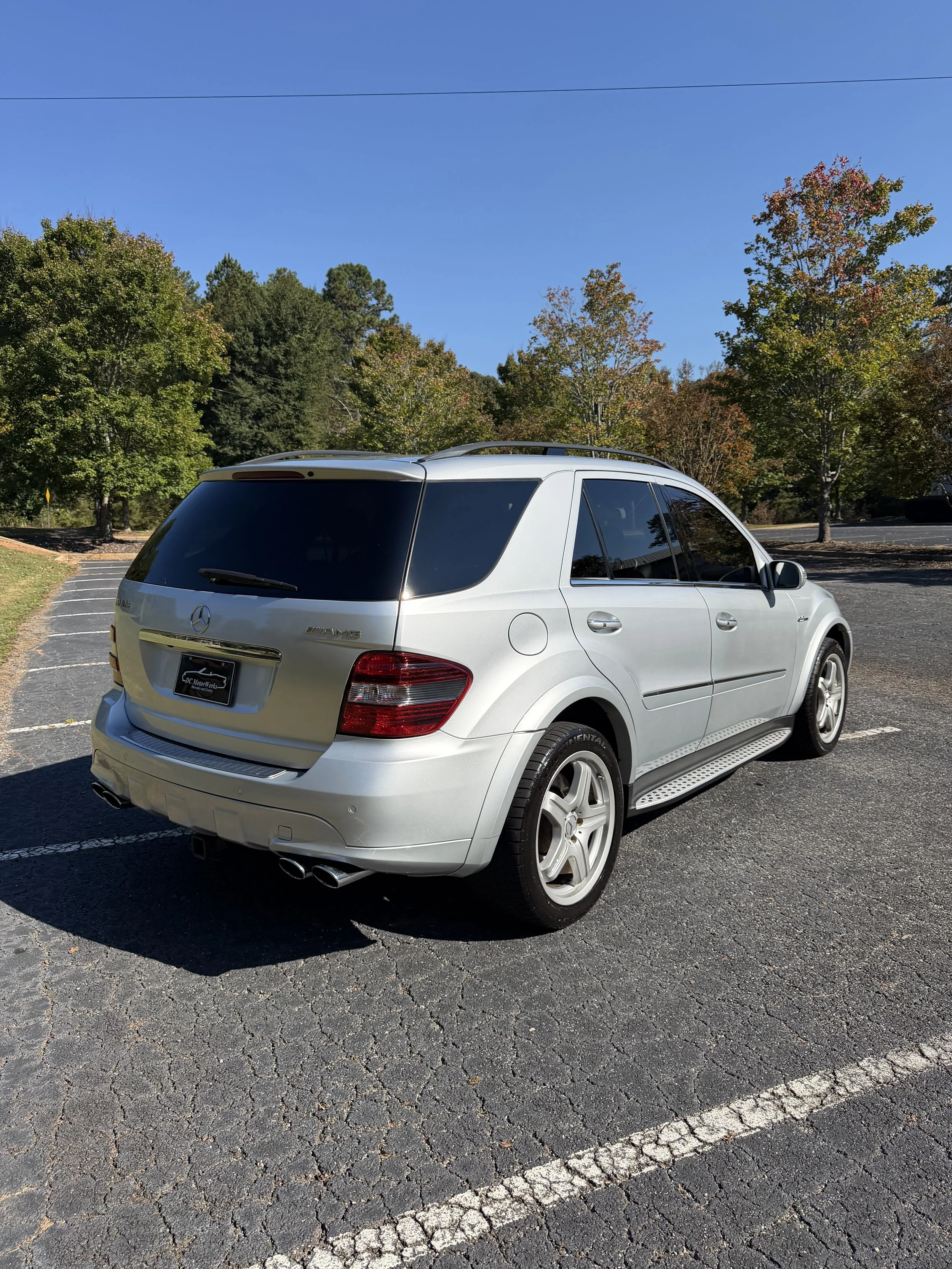 Close-up of the front part of a white Mercedes-Benz car, showing the wheel, part of the front bumper, and a badge that reads '6.3 AMG' on the side.