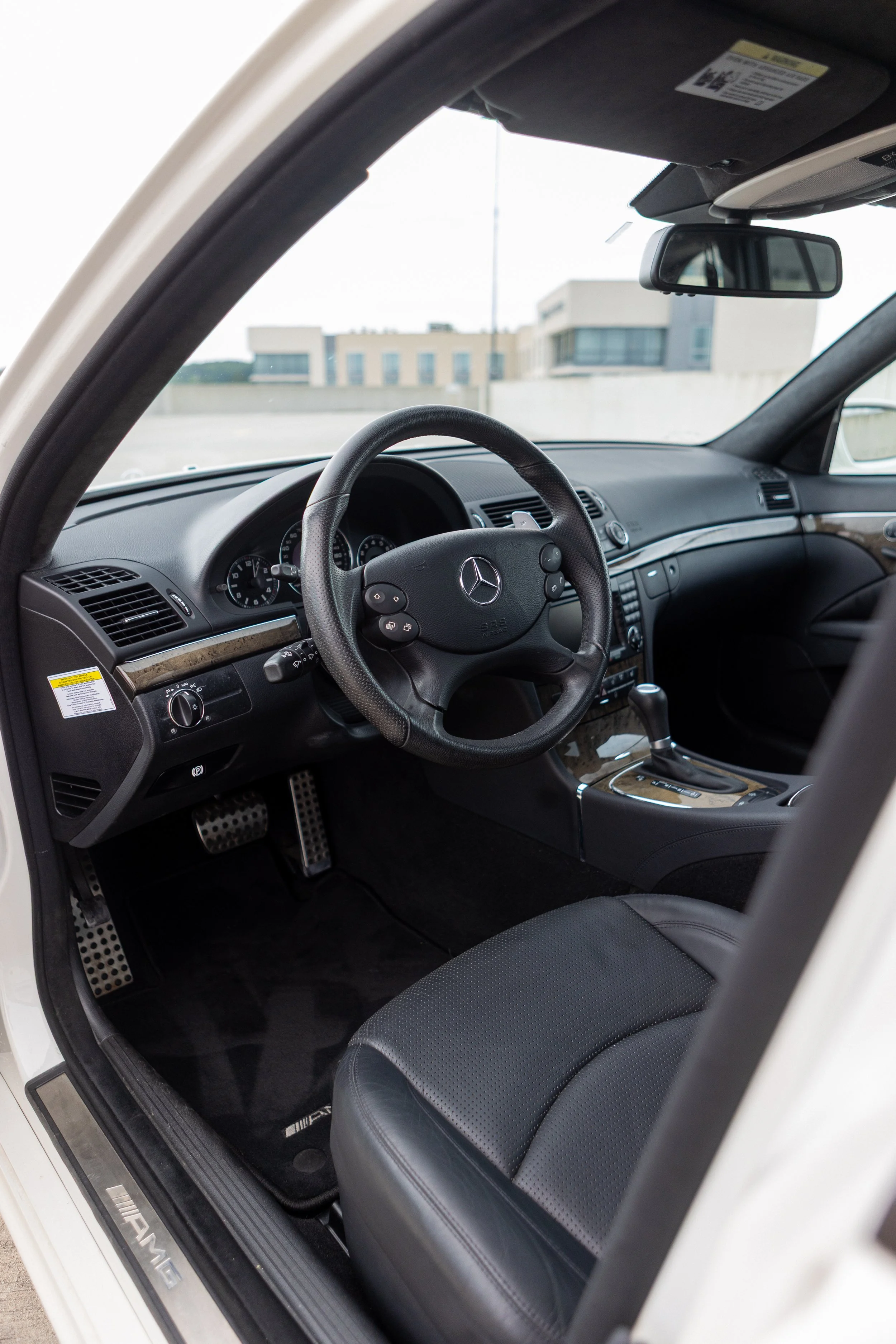 Interior of a luxury Mercedes-Benz vehicle showcasing the dashboard, steering wheel, and front seat, with a modern building visible through the windshield.