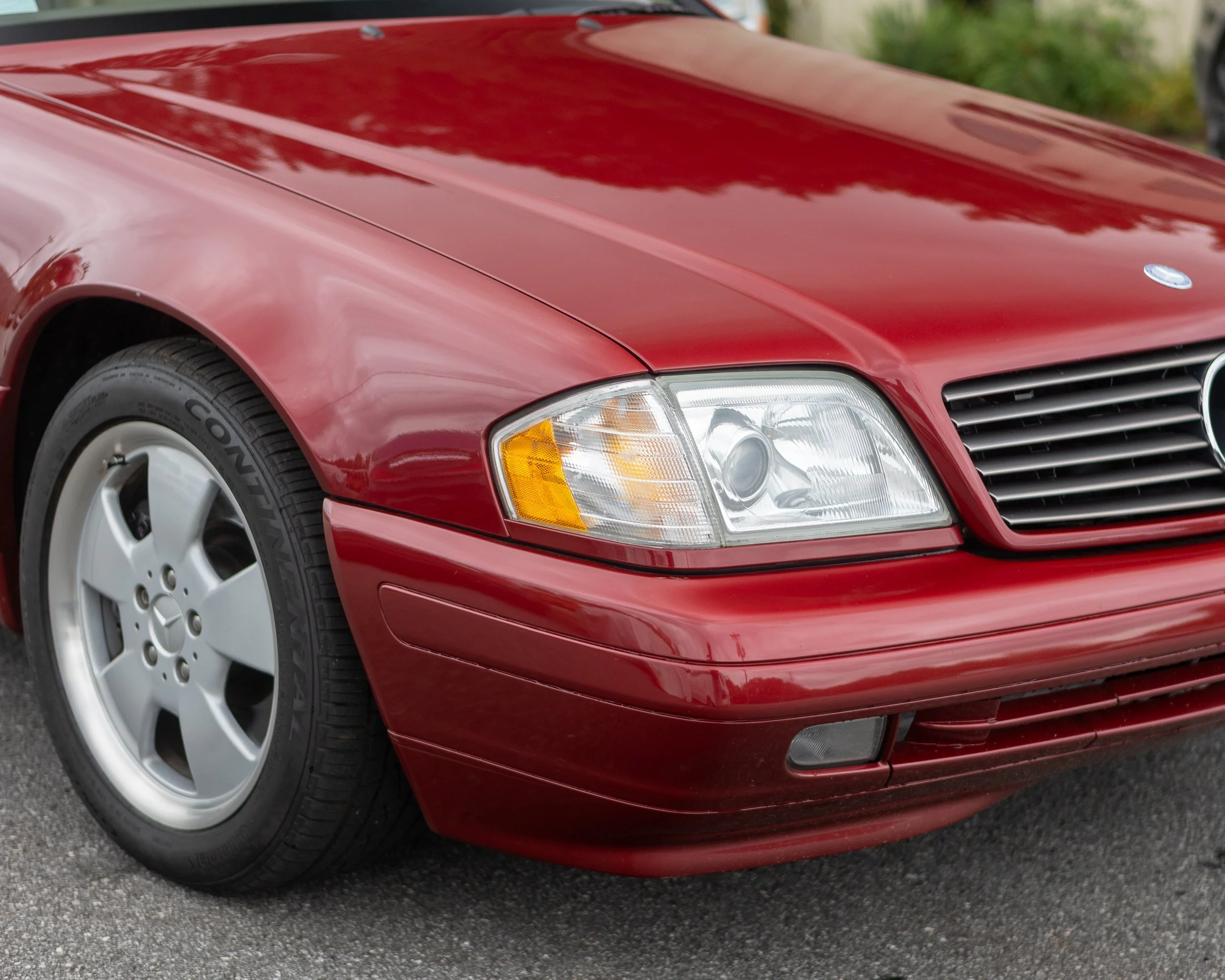 Close-up of the front part of a white Mercedes-Benz car, showing the wheel, part of the front bumper, and a badge that reads '6.3 AMG' on the side.