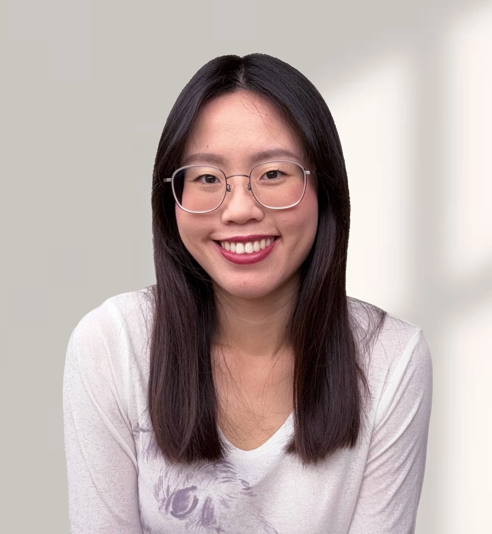 Portrait of a young Asian woman with long dark hair, wearing glasses and a light-colored top, smiling against a neutral background.