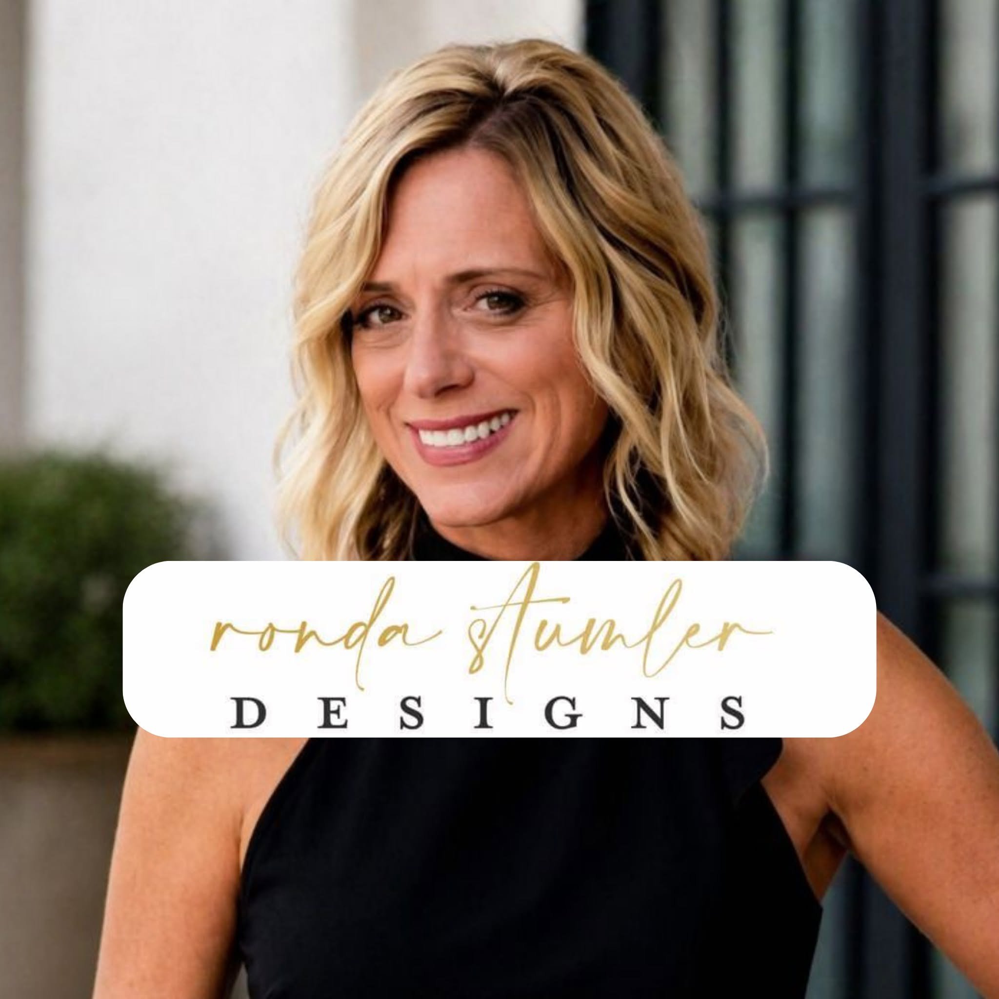 Close-up of a woman with blonde wavy hair wearing a black top that has text reading 'ronda stumper DESIGN'.