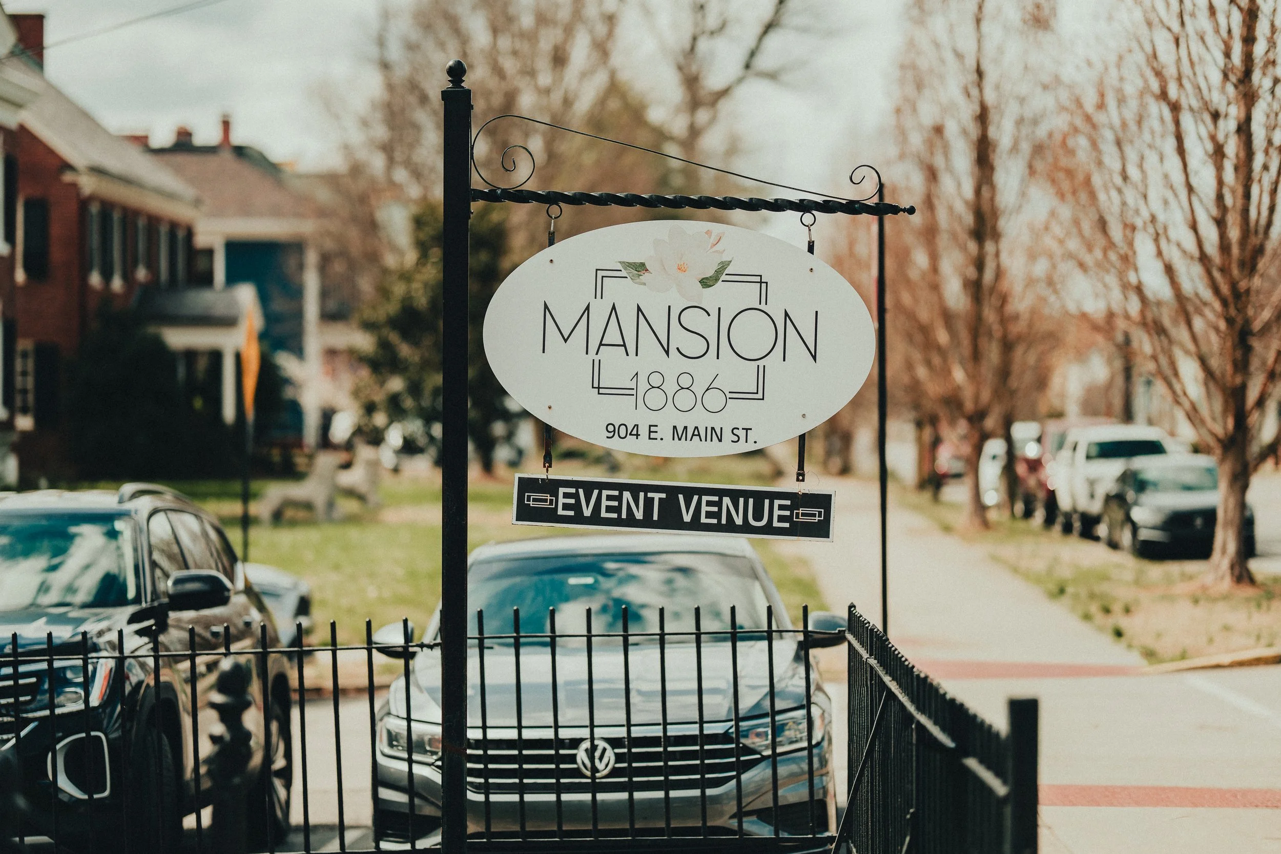 A street view showing a sign for 'Mansion 1886' and an event venue, with parked cars and leafless trees in the background.