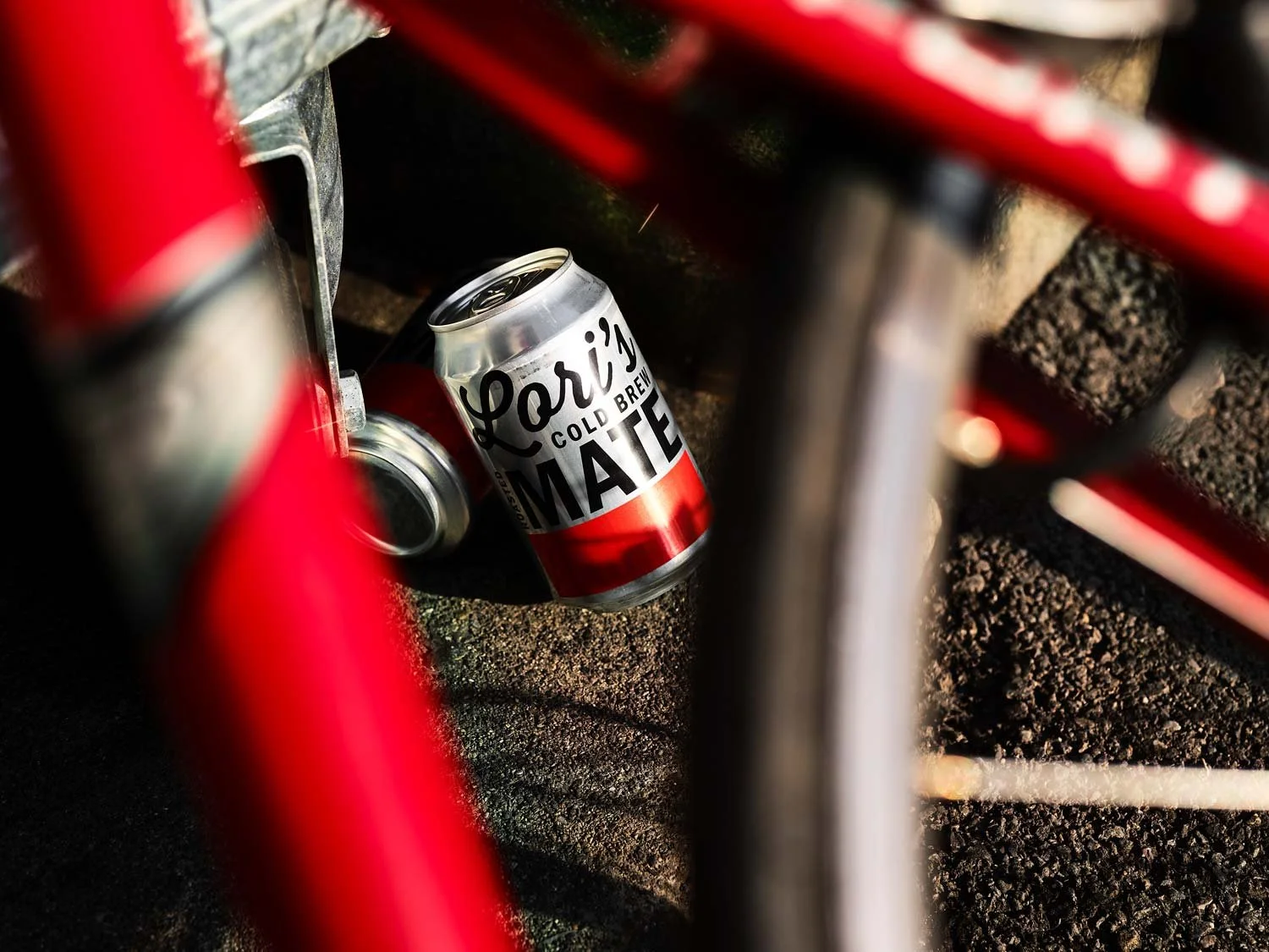 Eine Dose des Arizonic Cold Brew-Mate Getränks liegt auf dem Boden, eingekeilt zwischen einem roten Fahrradrahmen und einem Schatten auf Asphalt.