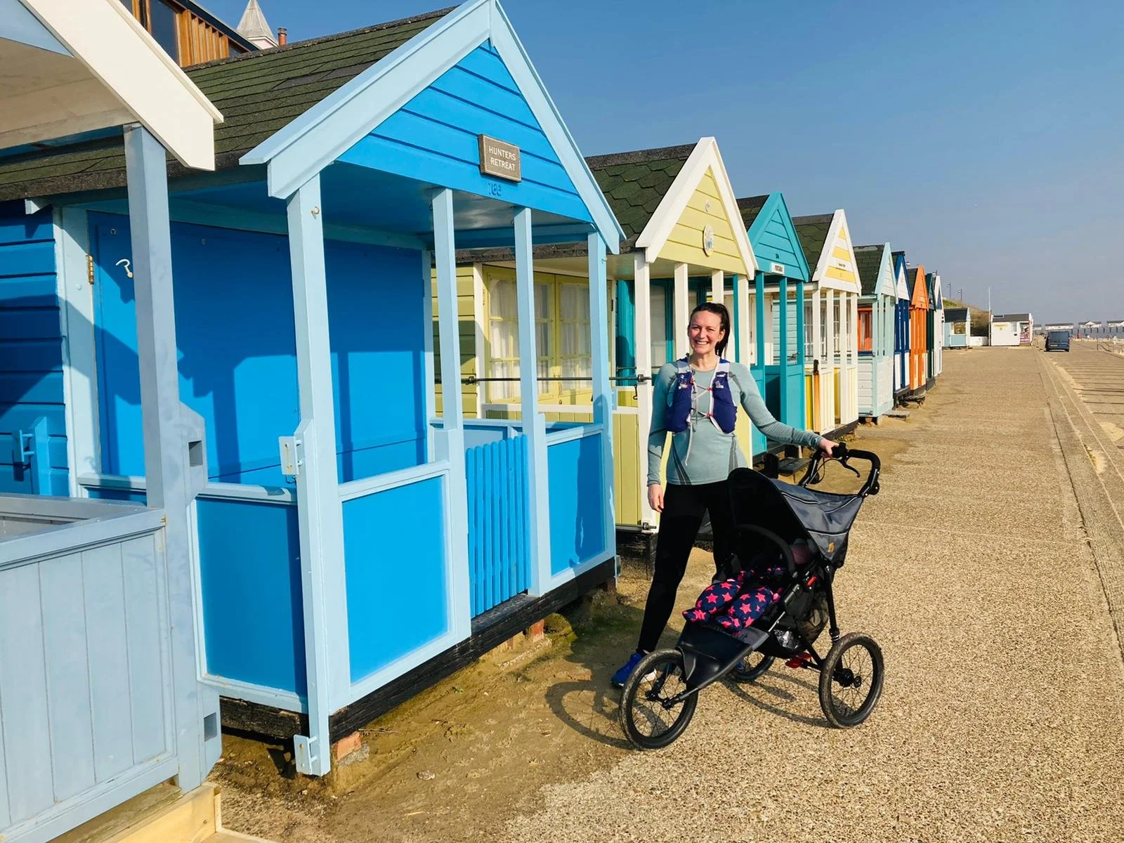 Run Collective team member cycling along the UK coastline near colourful beach huts during a corporate wellness break.