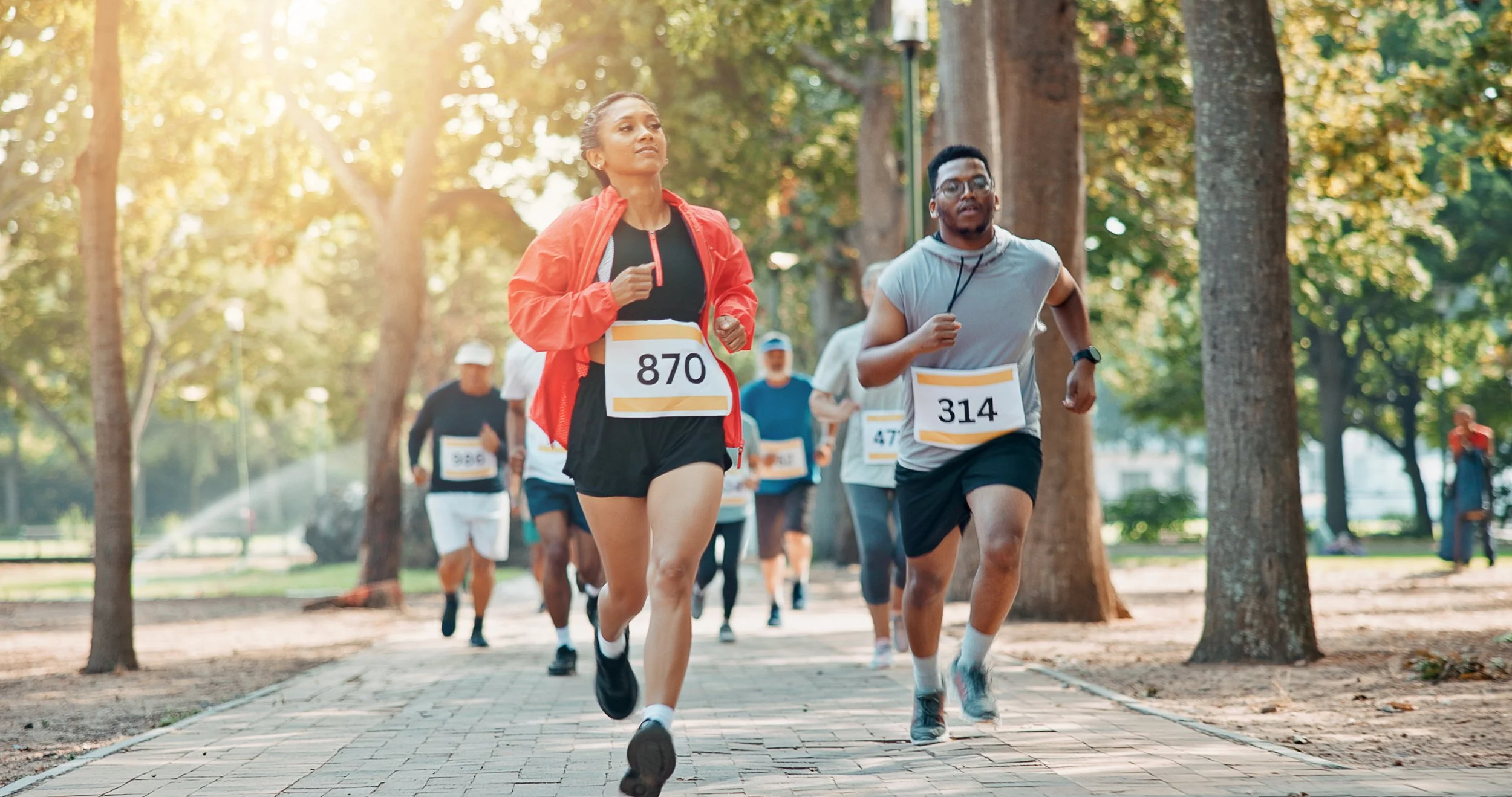 Run Collective UK corporate runners racing through a park with race bibs during autumn