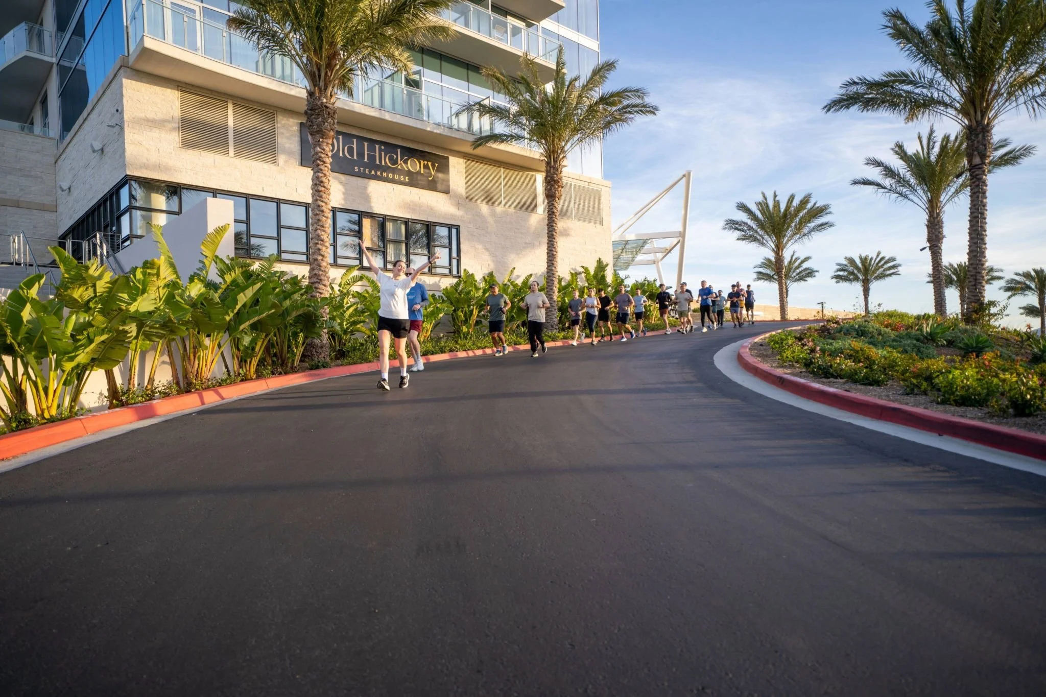 Team members running along a palm-lined waterfront road during a corporate running event.