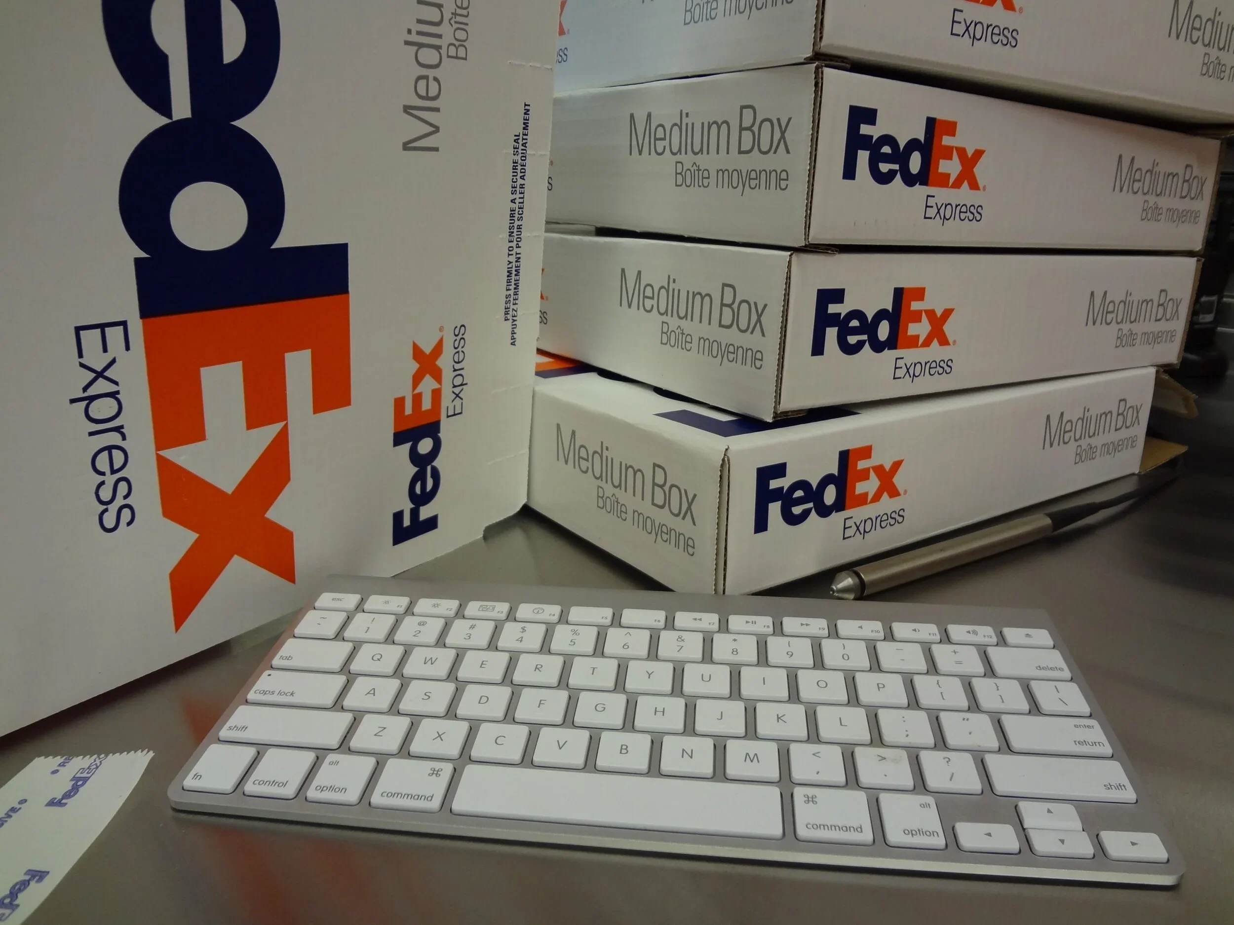 Stacked FedEx Express medium boxes on a desk with a white computer keyboard in the foreground.