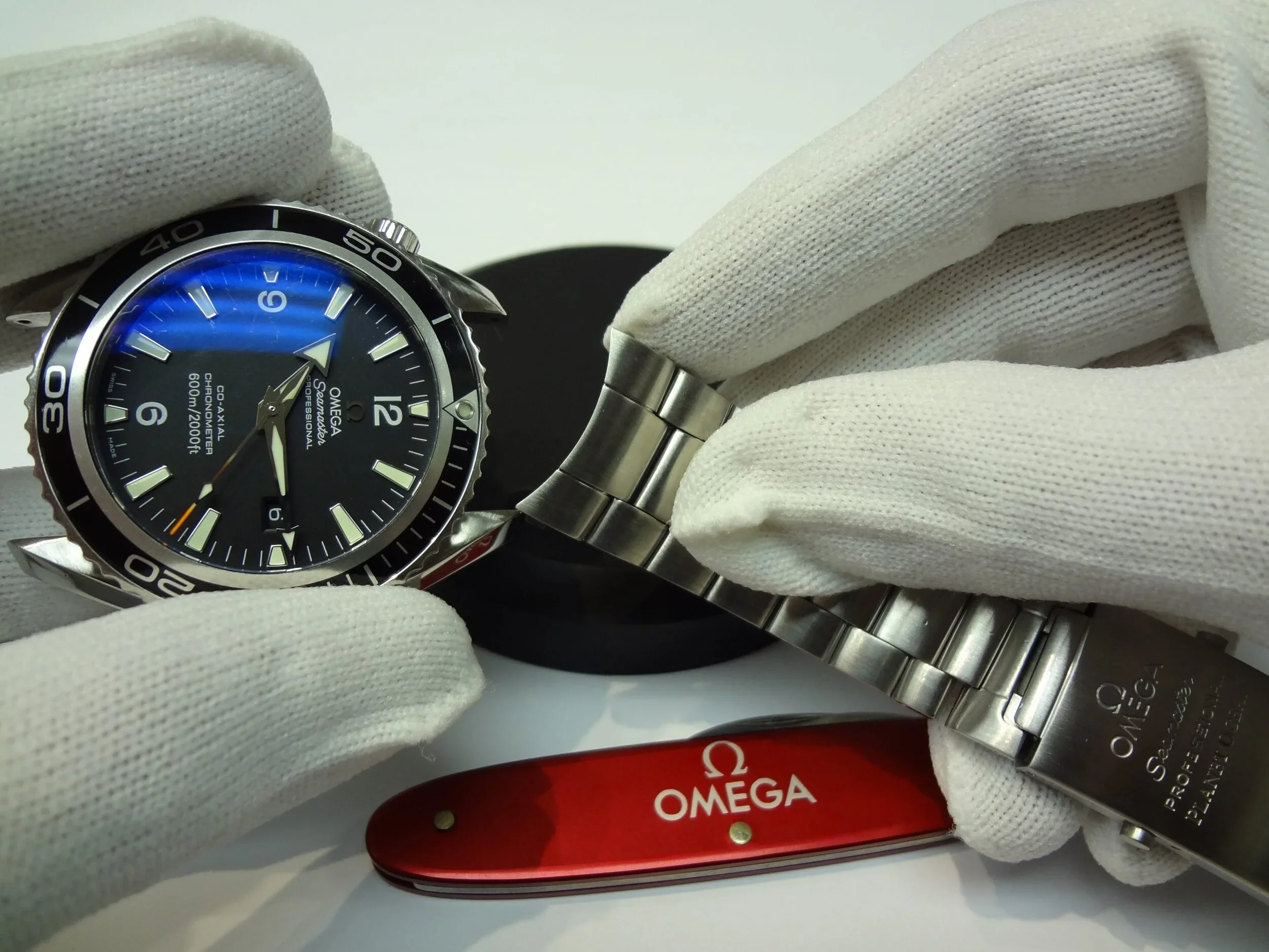 Close-up of a person wearing white gloves holding a black Omega Seamaster Professional wristwatch with a stainless steel bracelet.