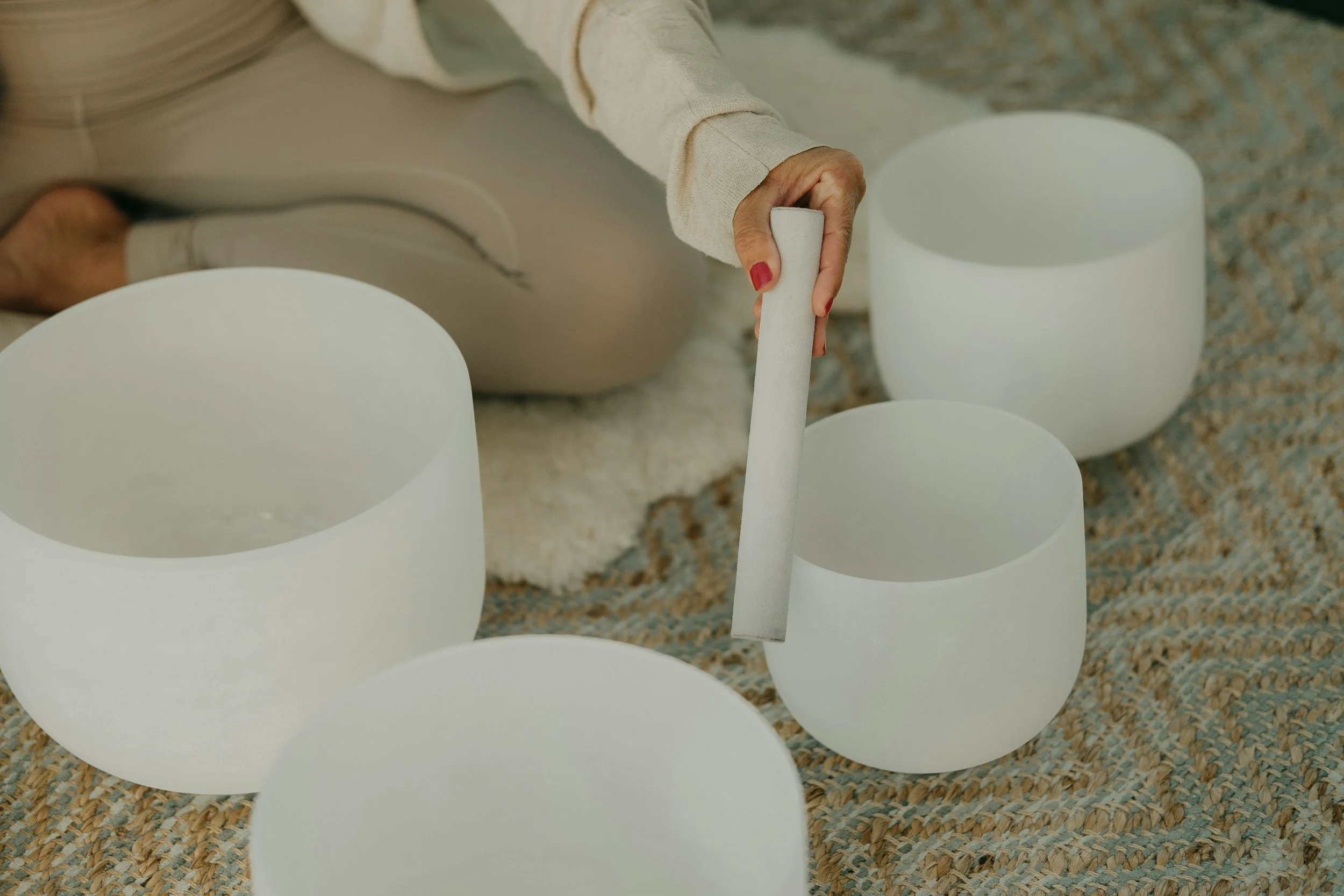 A person playing a wind instrument, possibly a pan flute, among several large white, cylindrical objects on a patterned carpeted floor.