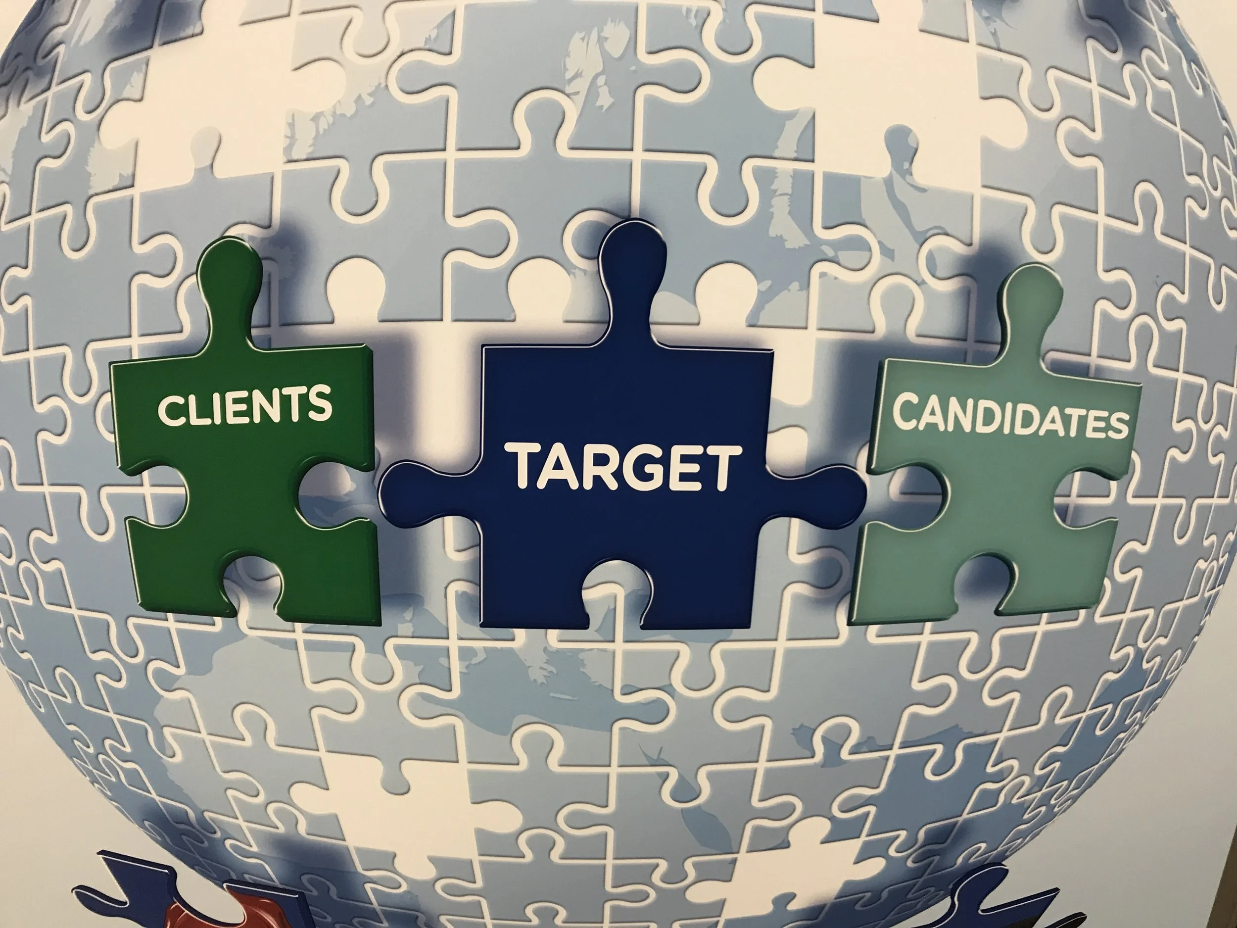 A globe-shaped puzzle with pieces labeled 'Clients', 'Candidates', and 'Target', with an image of the world in the background.